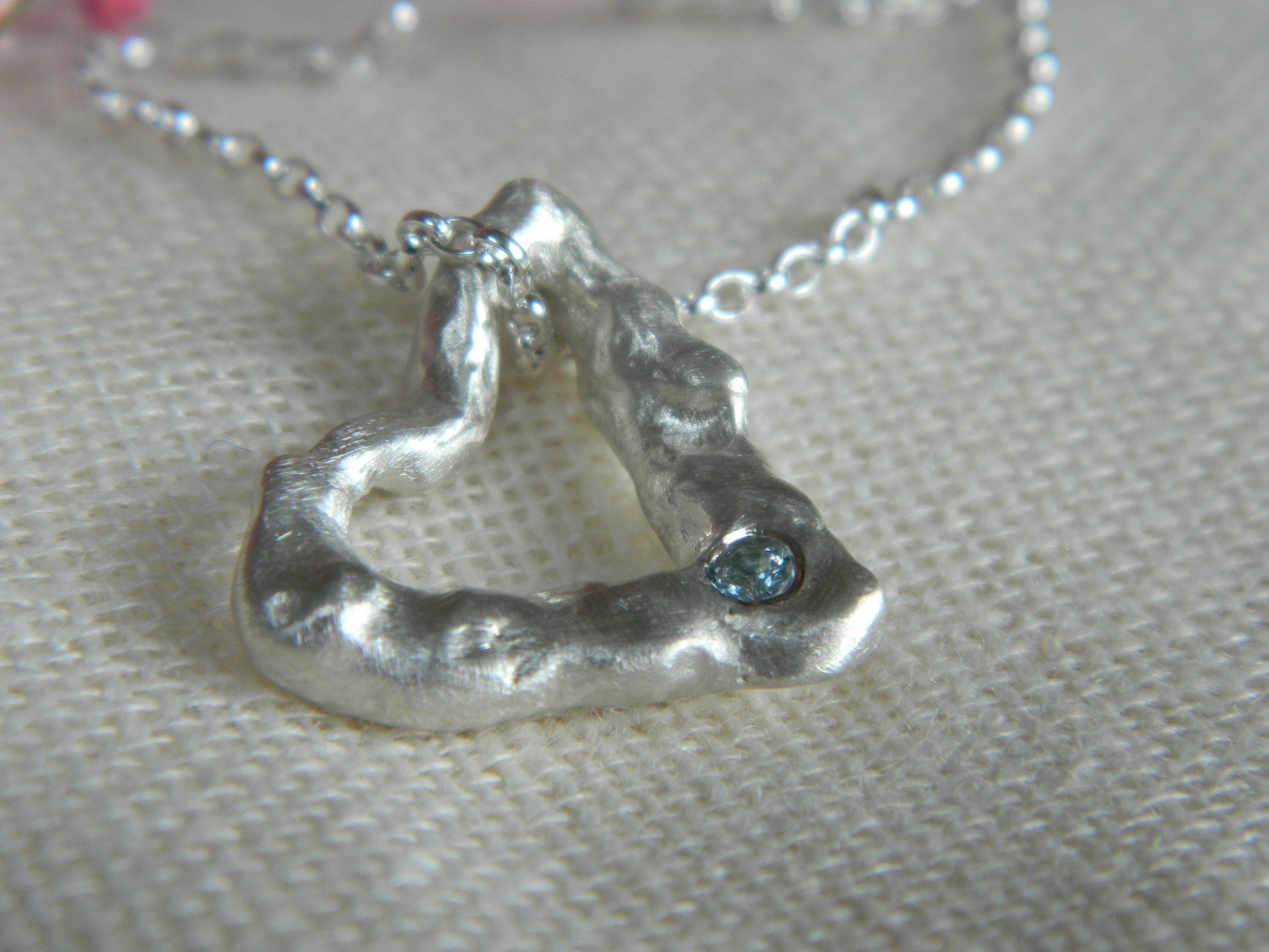 Handmade in sterling silver with flowing, organic textures. A unique statement molten heart pendant offering passion, artistry, and a sustainable design, including a flush set aquamarine..