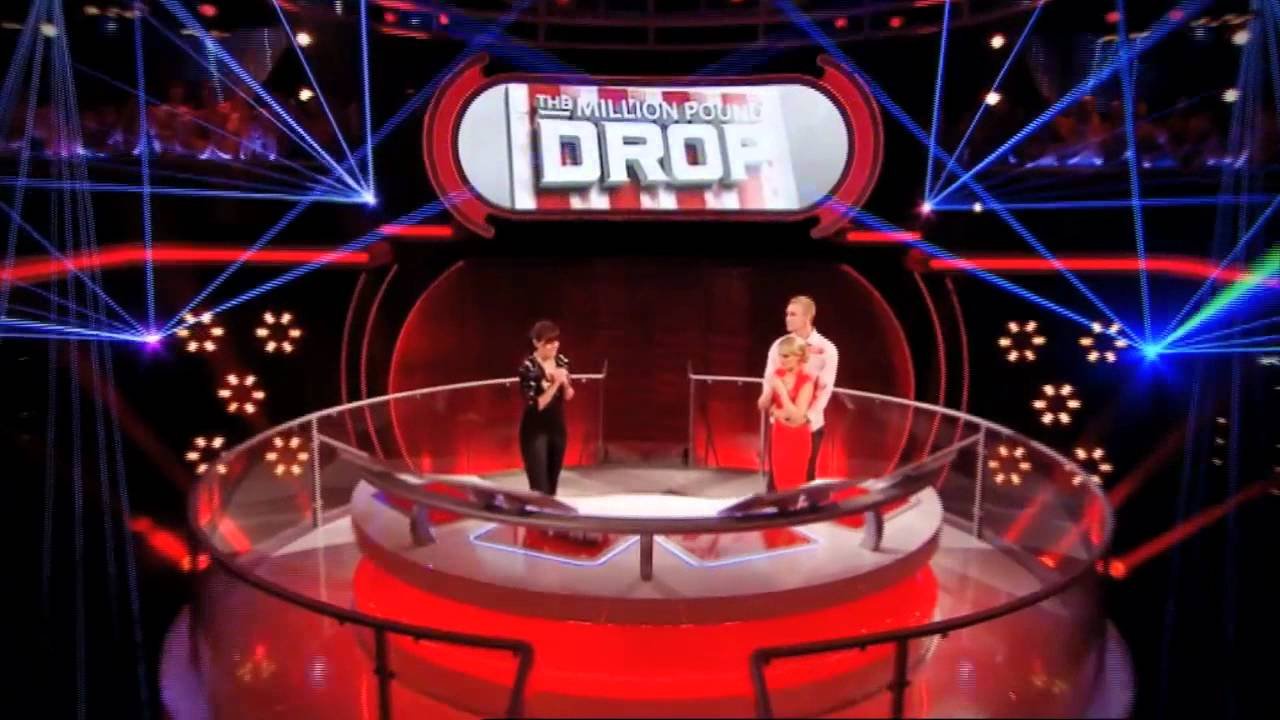 TV game show set, vibrant lighting, large digital screen displaying "The Million Pound Drop," featuring a host and contestants.