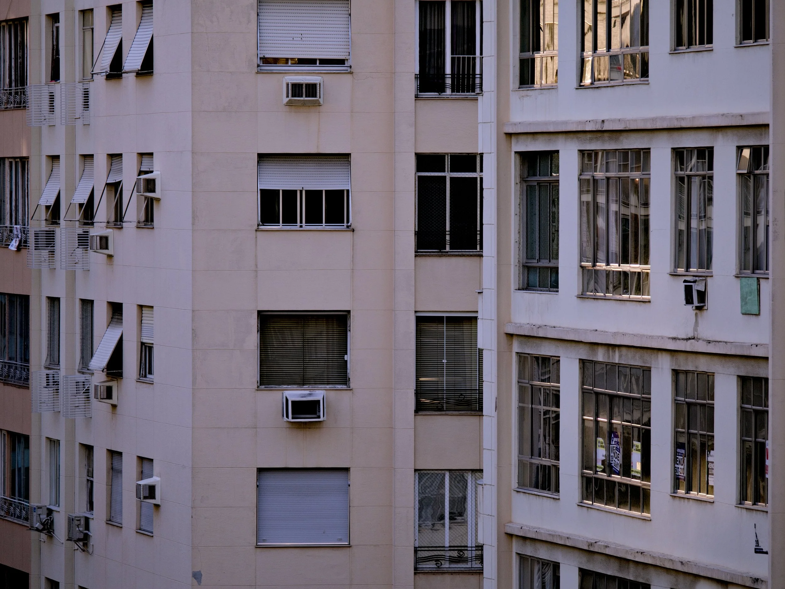 A zoomed in image of the details of an apartment building, showing windows, AC, and other elements of the building facade.