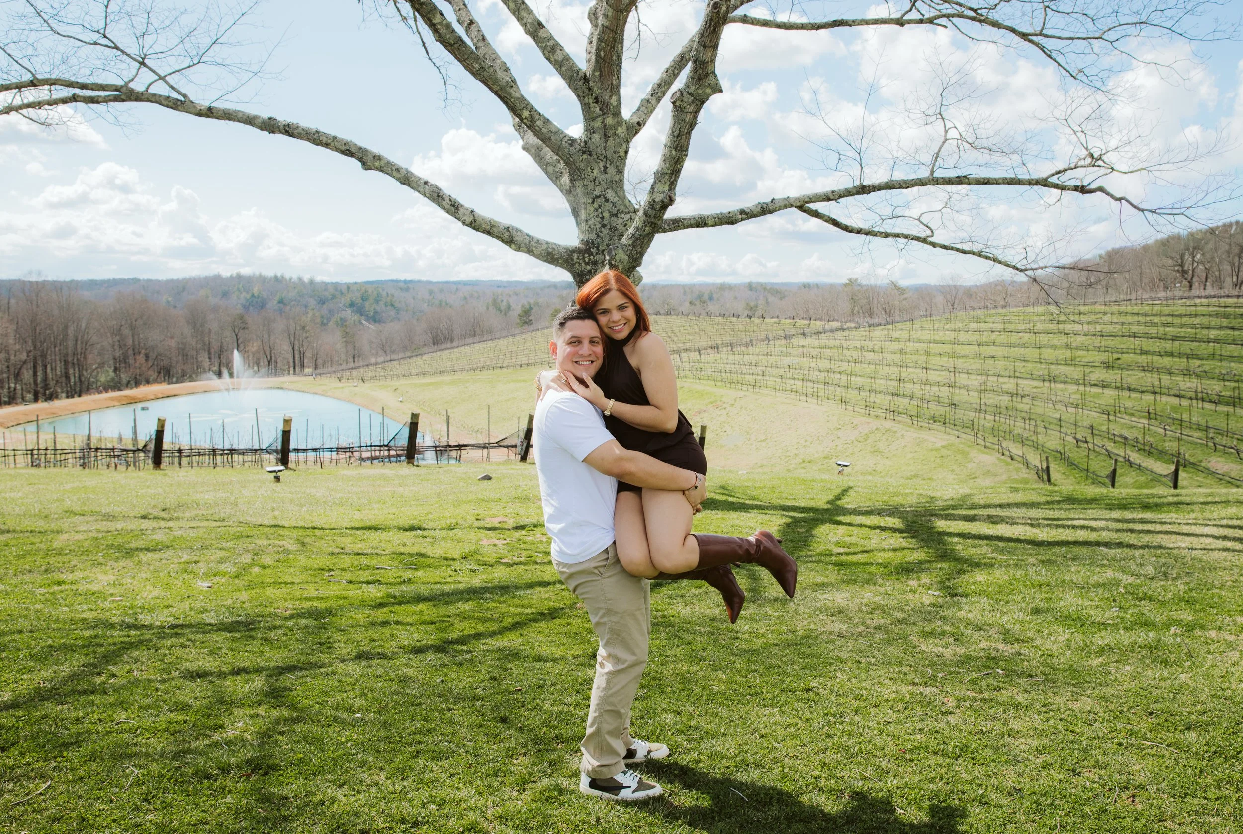  A man lifting his fiancée in the air with the rolling hills and vineyards of Montaluce Winery 