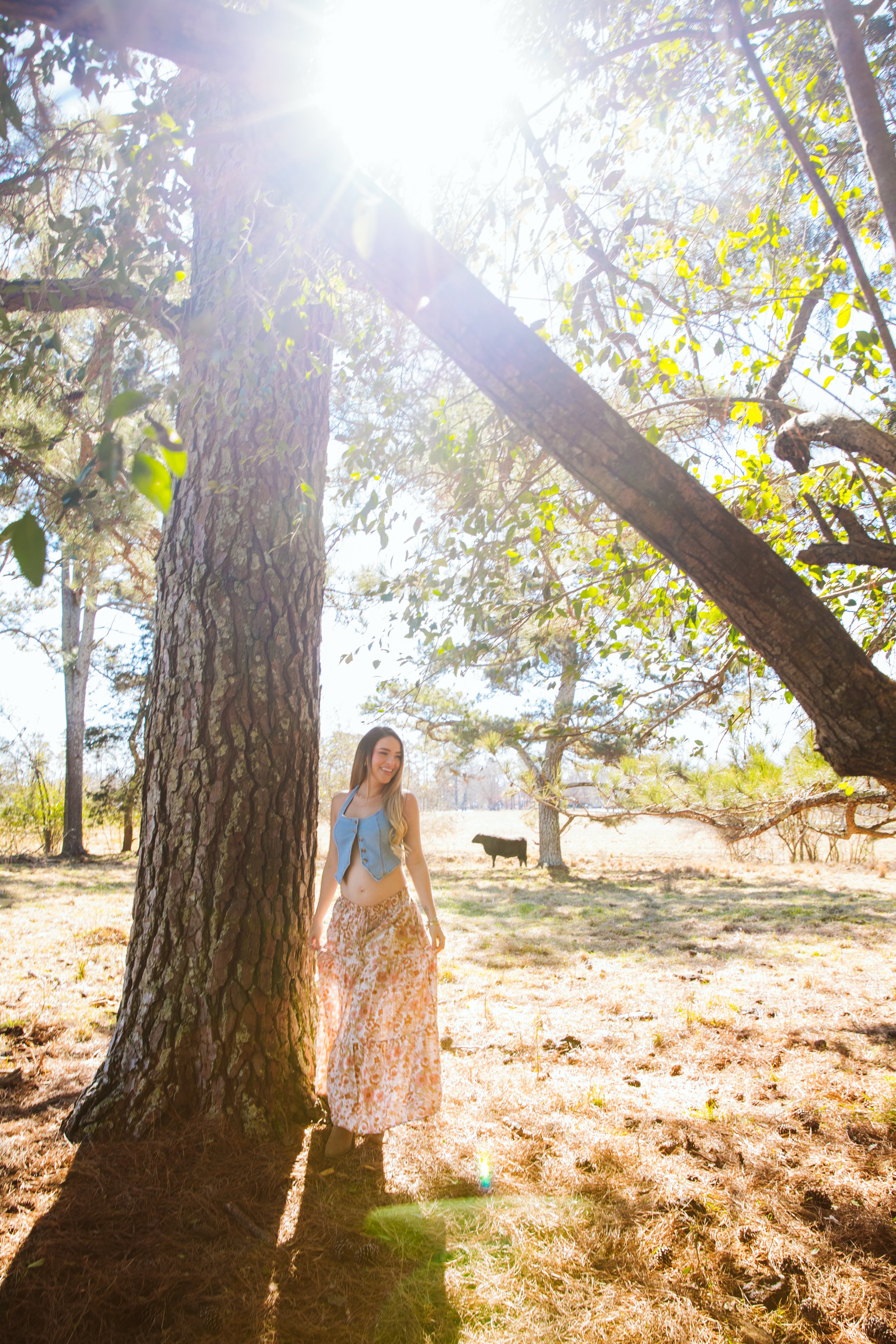 Outdoor portrait of woman standing beside large tree in golden sunlight