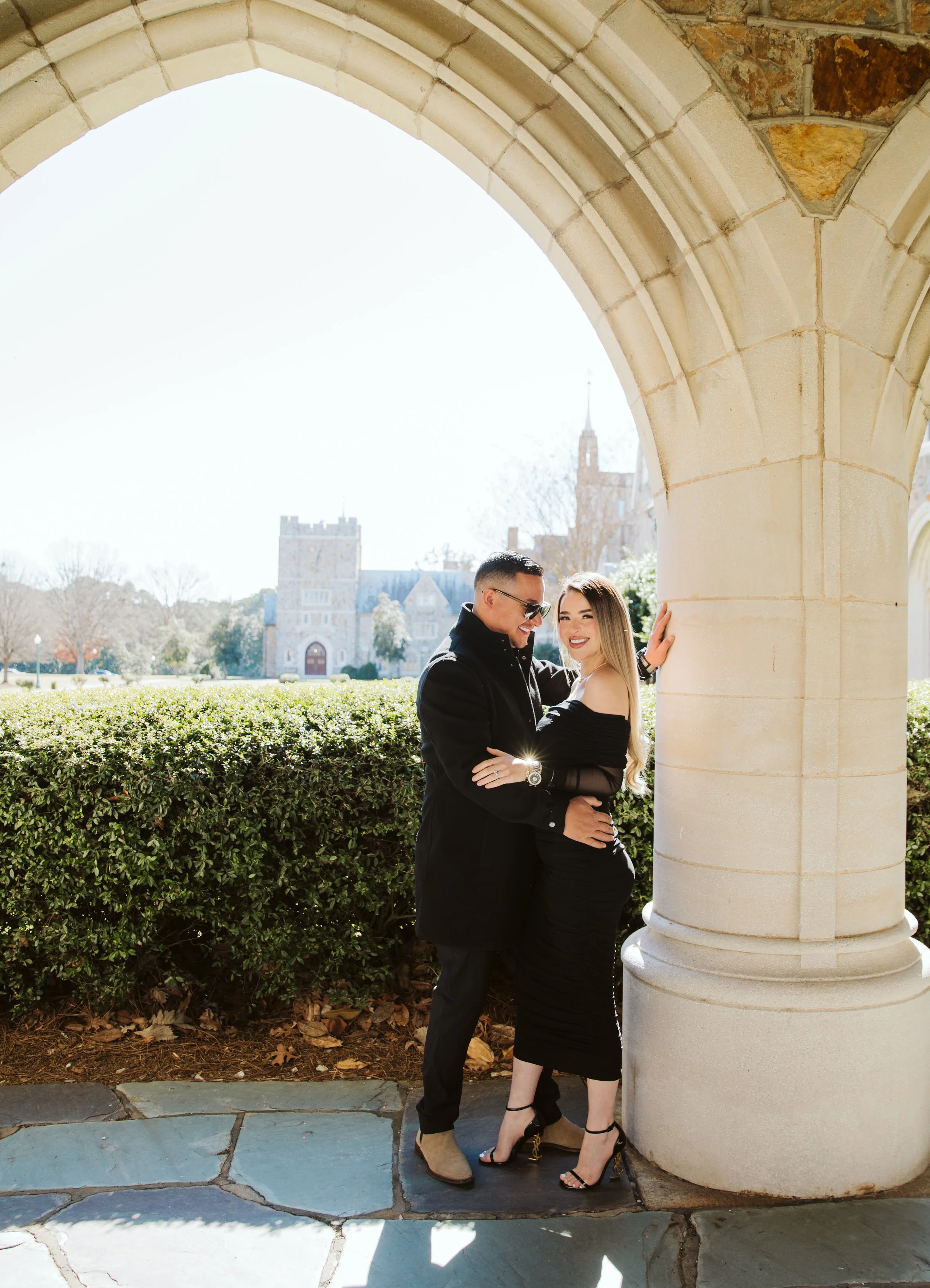 Elegant couple portrait under historic archway at university campus