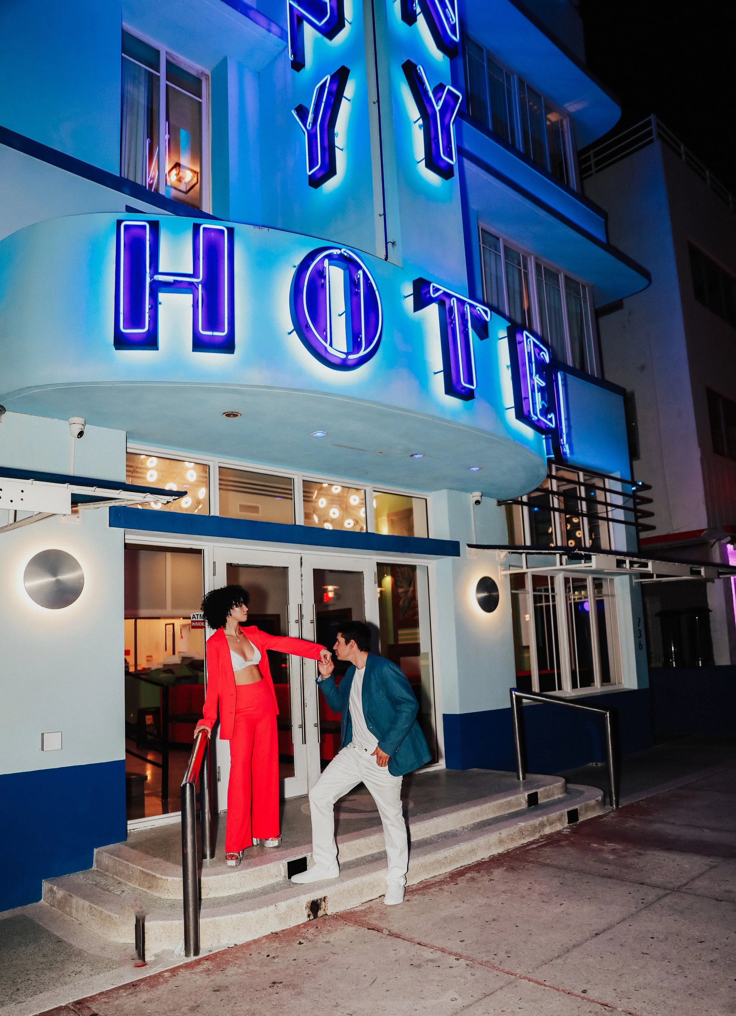 Couple posing under neon hotel sign entrance