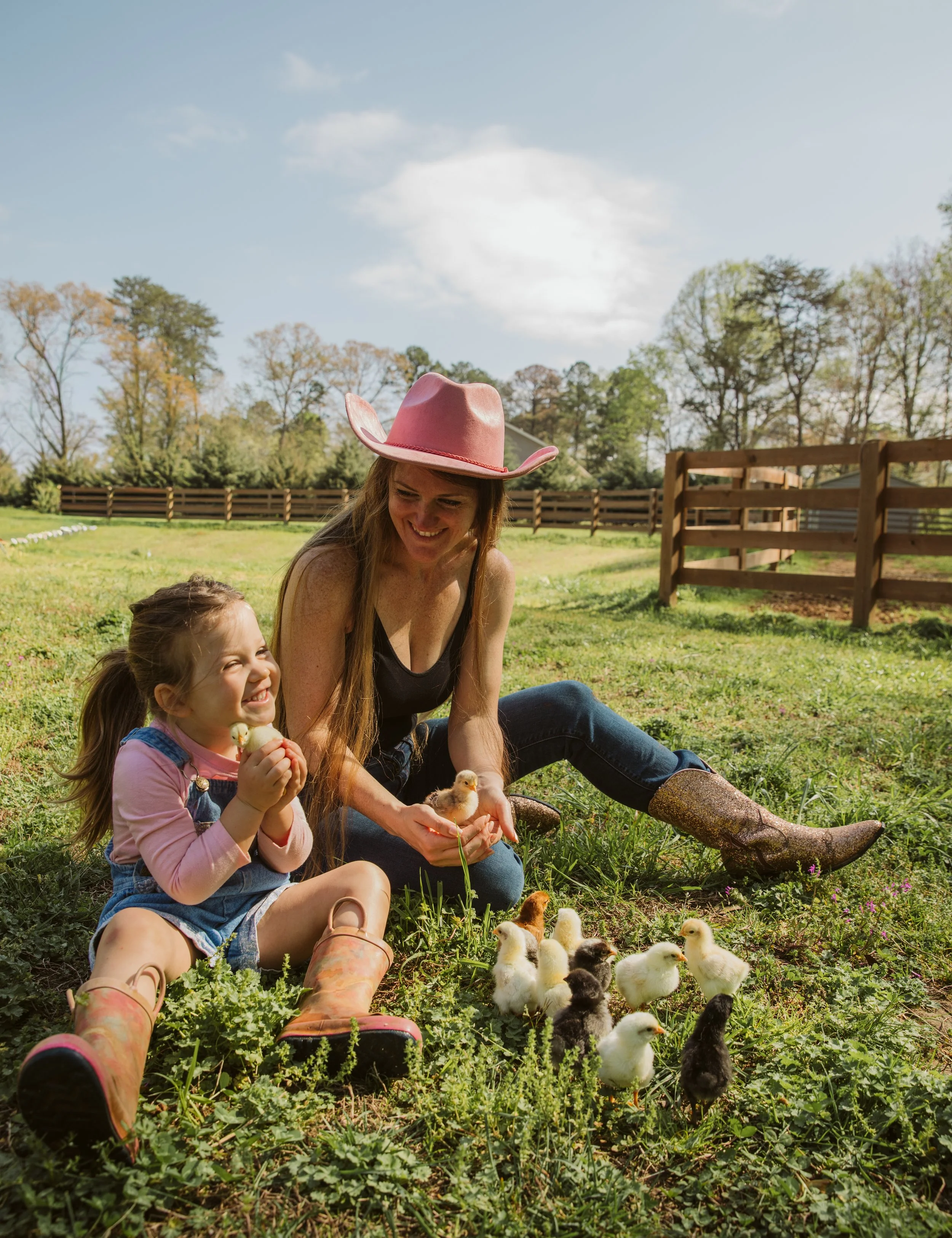 Mom and daughter sitting in grass with baby chicks