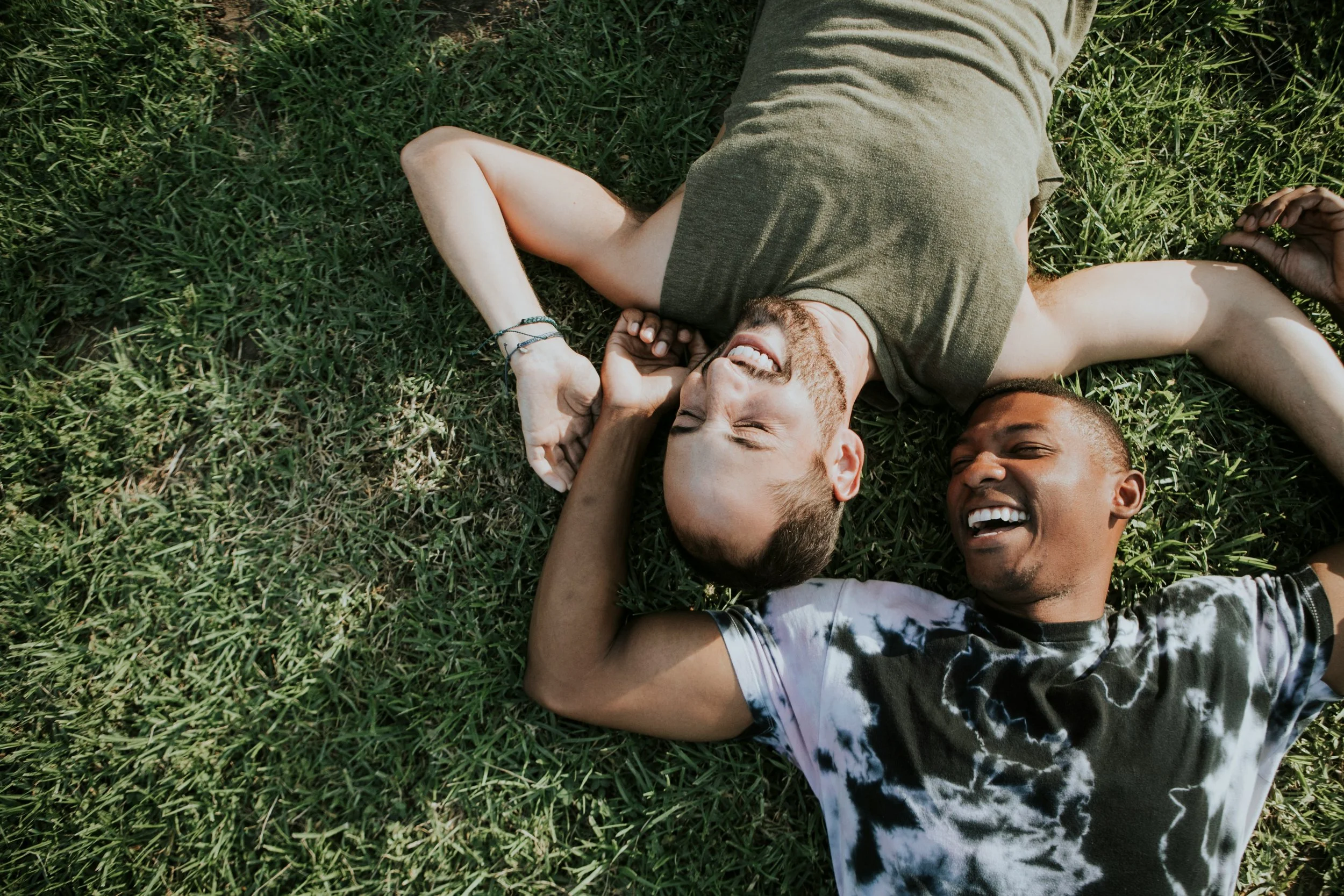 Two young men lying on grass, smiling and enjoying each other's company.