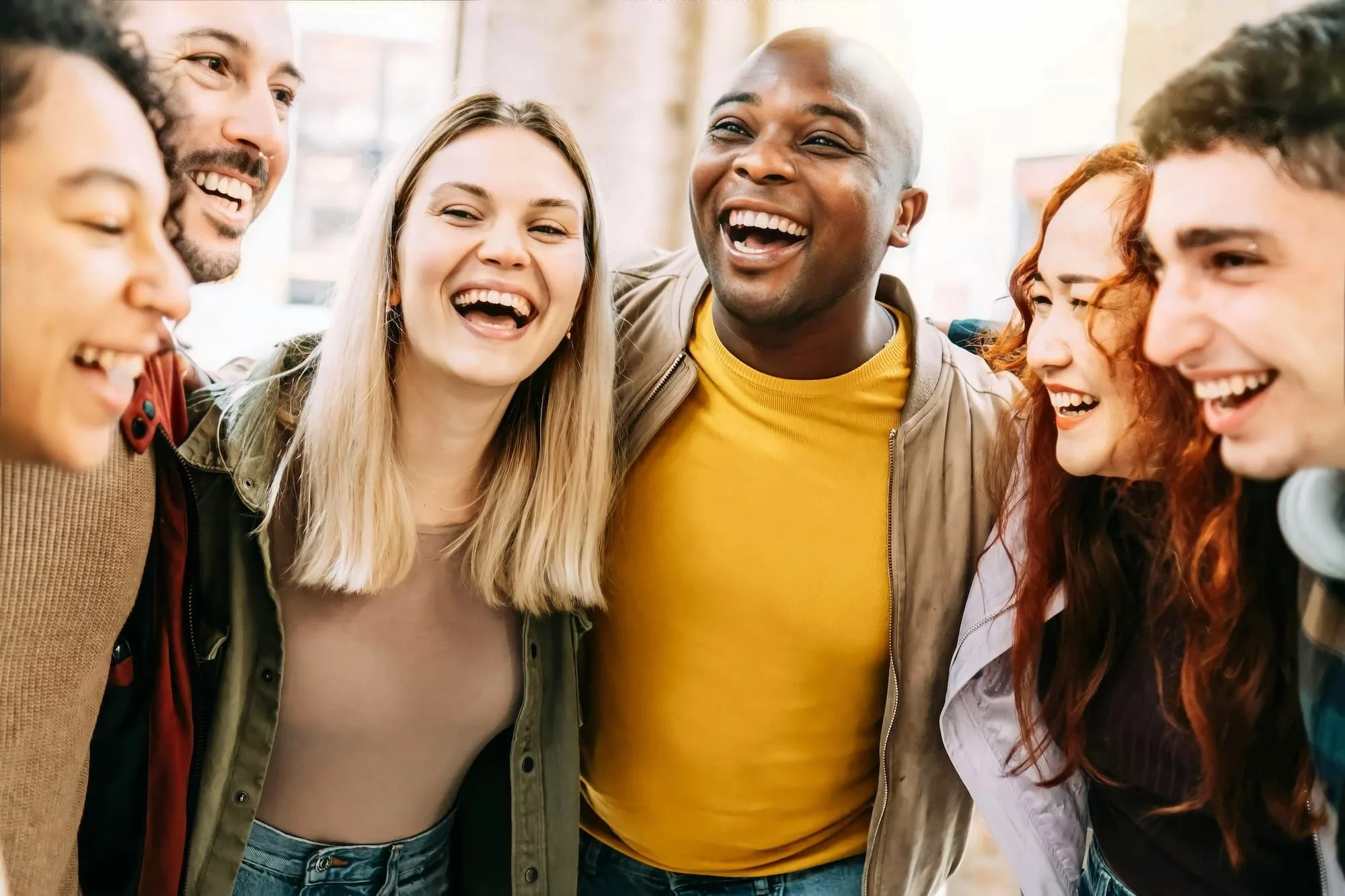 A group of diverse adults smiling and laughing together in a close circle.