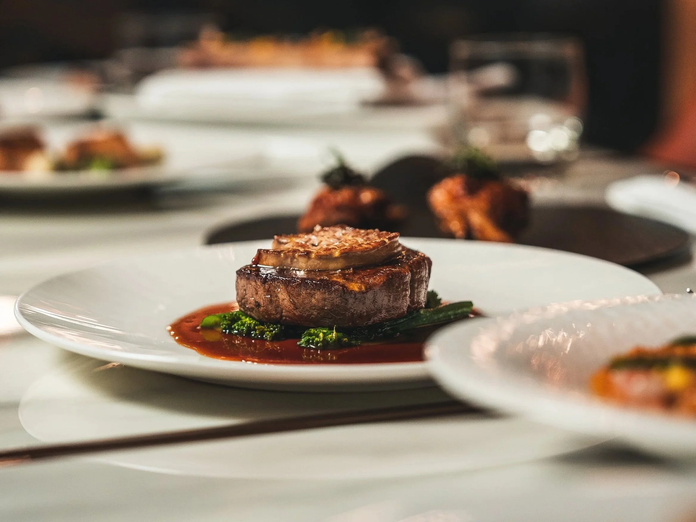 An artisan wagyu steak with sauce and vegetables, close-up on a white plate, fine dining cuisine.
