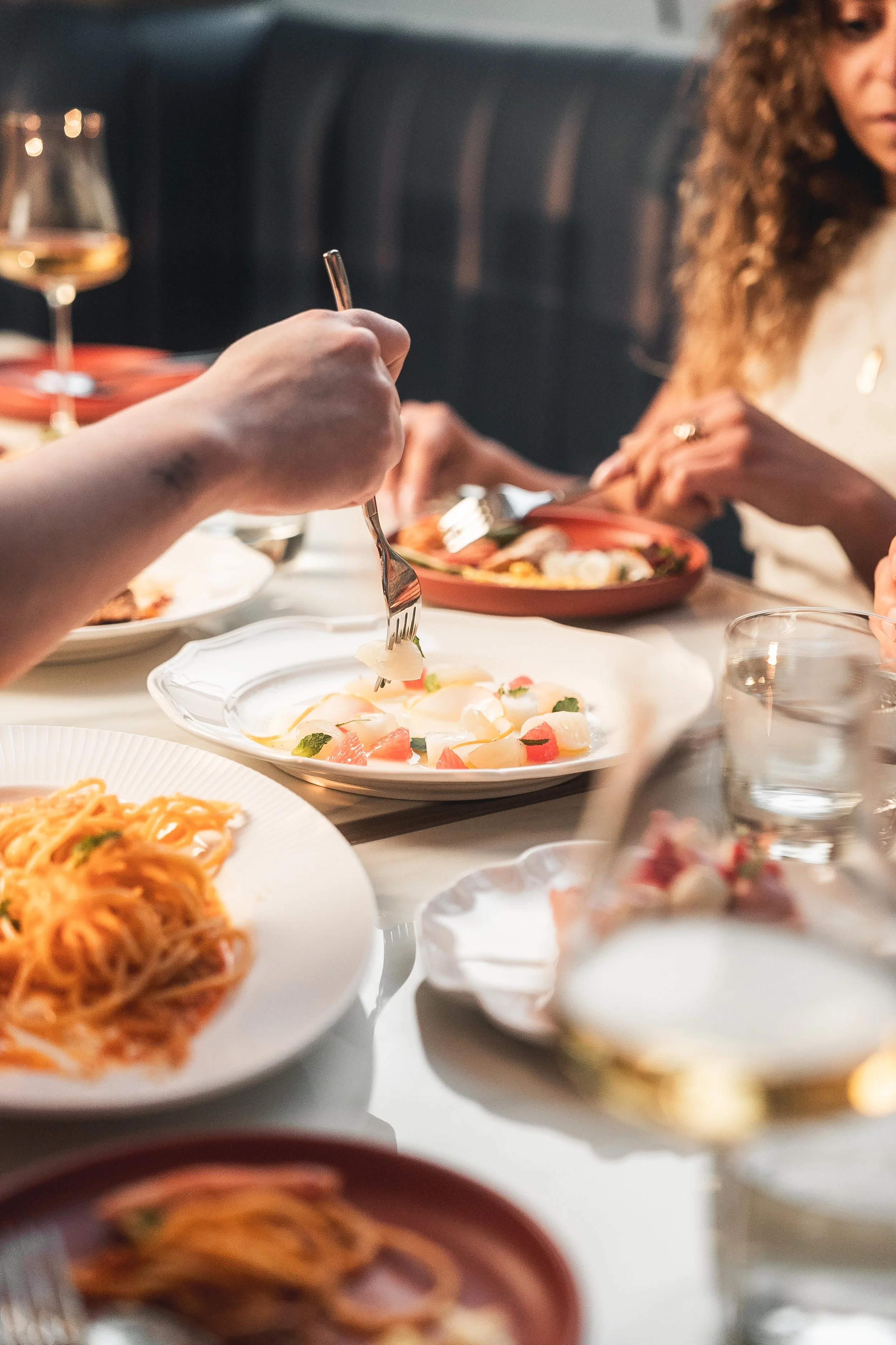 People enjoying a meal with various dishes, including pasta, salad, and drinks, on a dining table.
