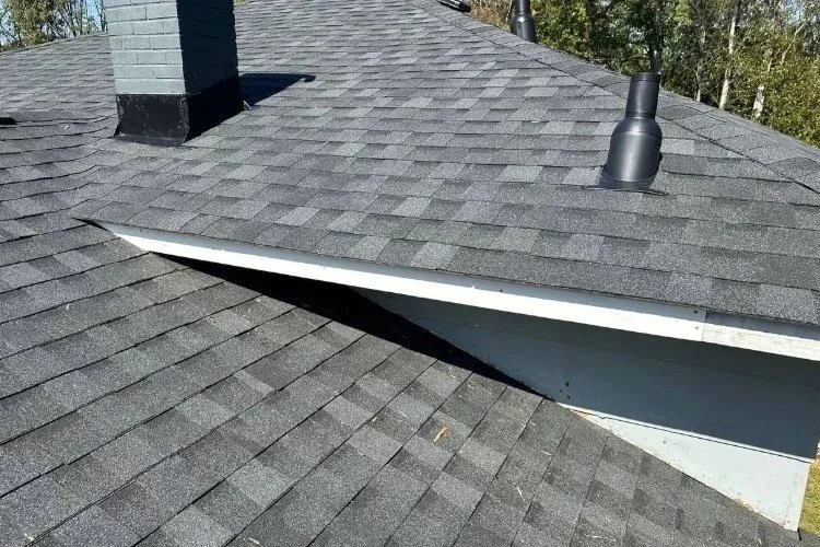 Close-up view of a gray shingle roof with a chimney and two vent pipes.