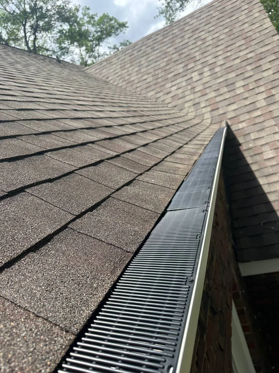 Close-up of a sloped residential roof with asphalt shingles and a metal gutter.