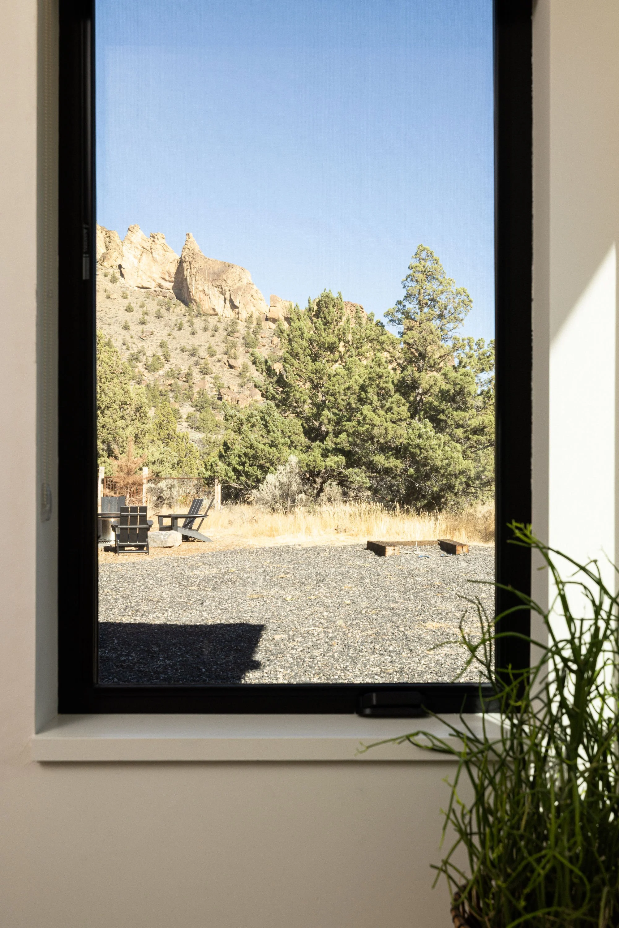 View through a window showing a mountainous landscape with rocks, trees, and a clear blue sky.