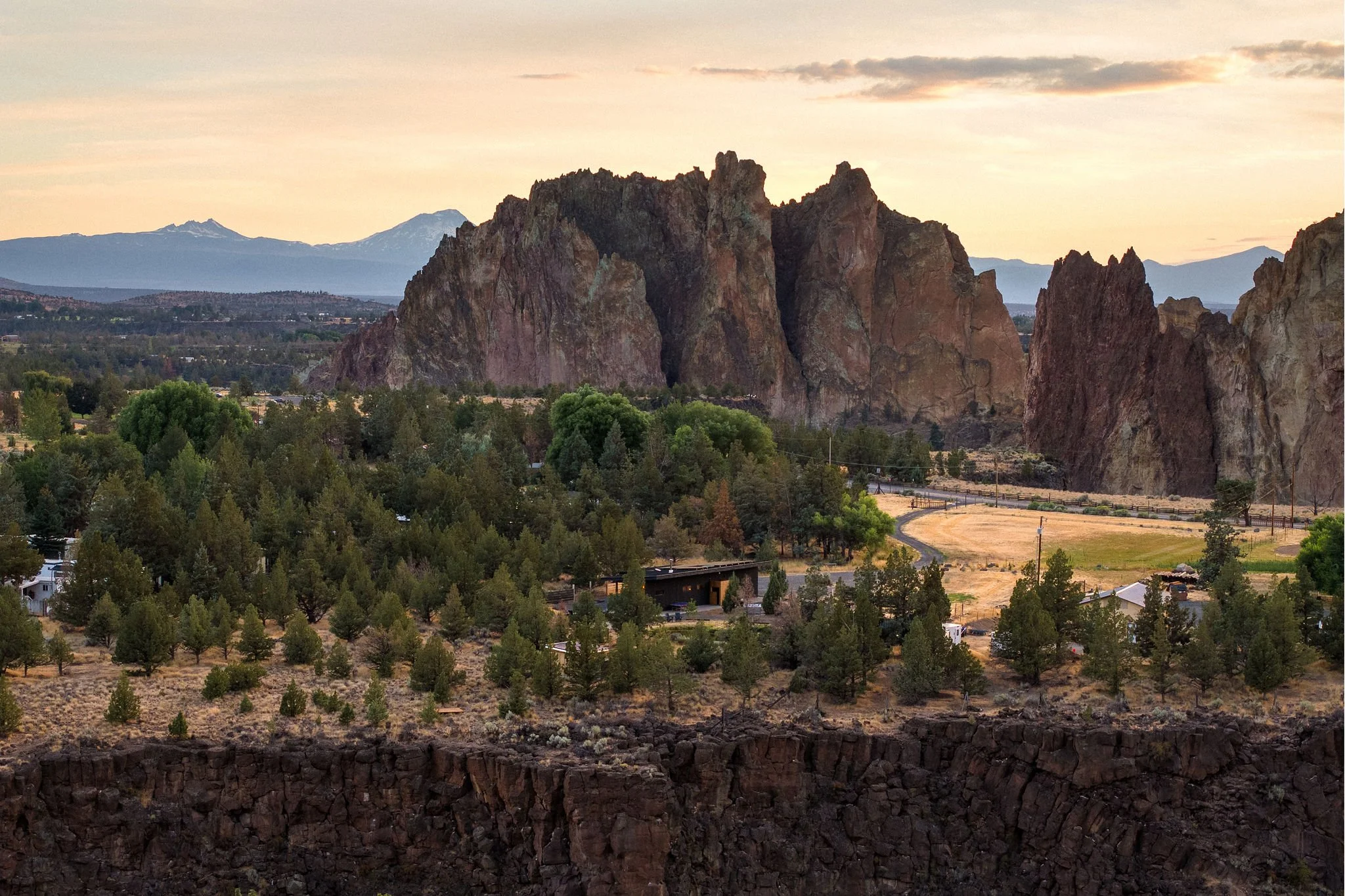 Scenic view of a mountainous landscape with large rock formations, trees, and a small residential area at sunset or sunrise.