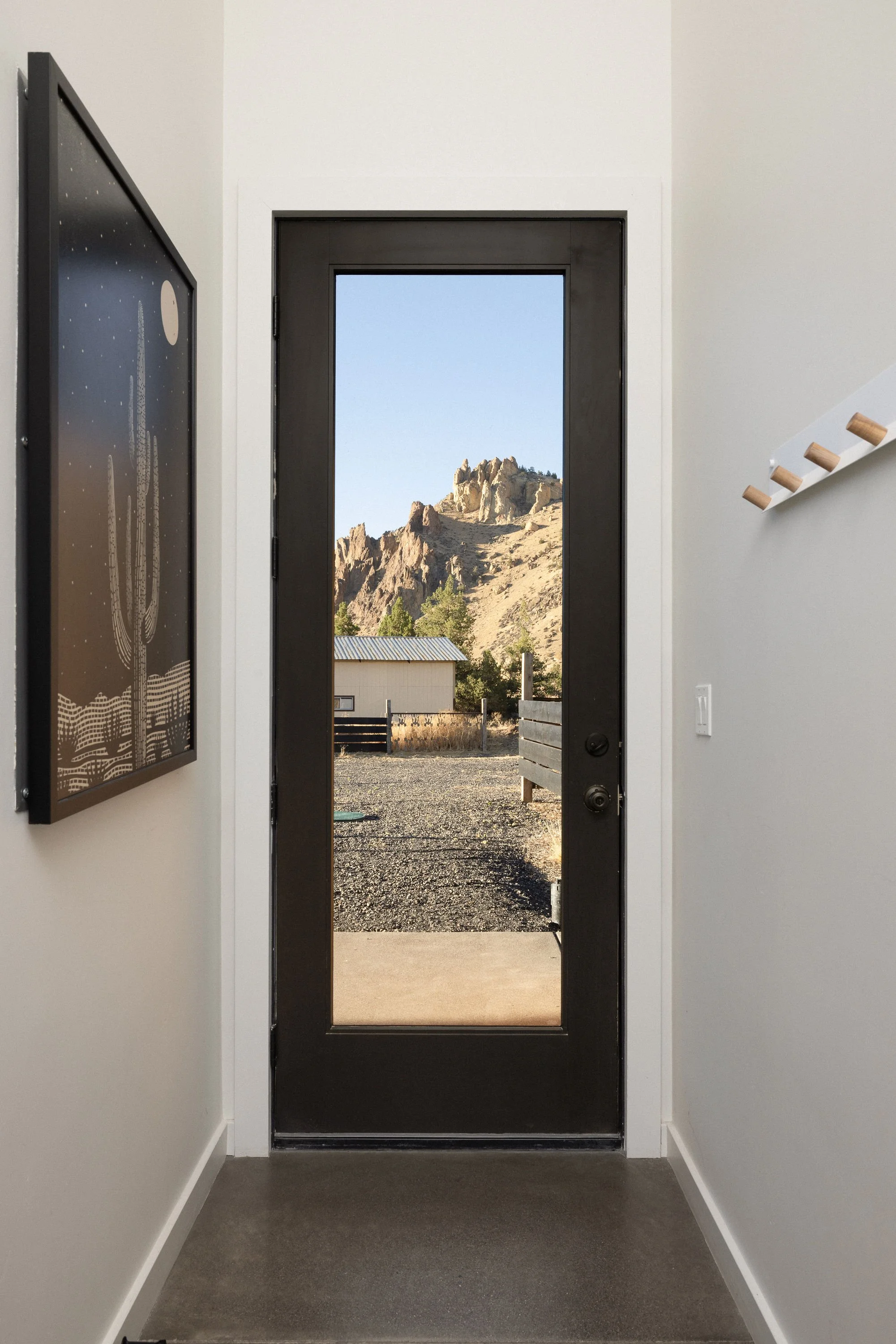 Interior view of a house entryway with a black door that has a large window, leading outside to a mountainous landscape with rocks, trees, and a small building.