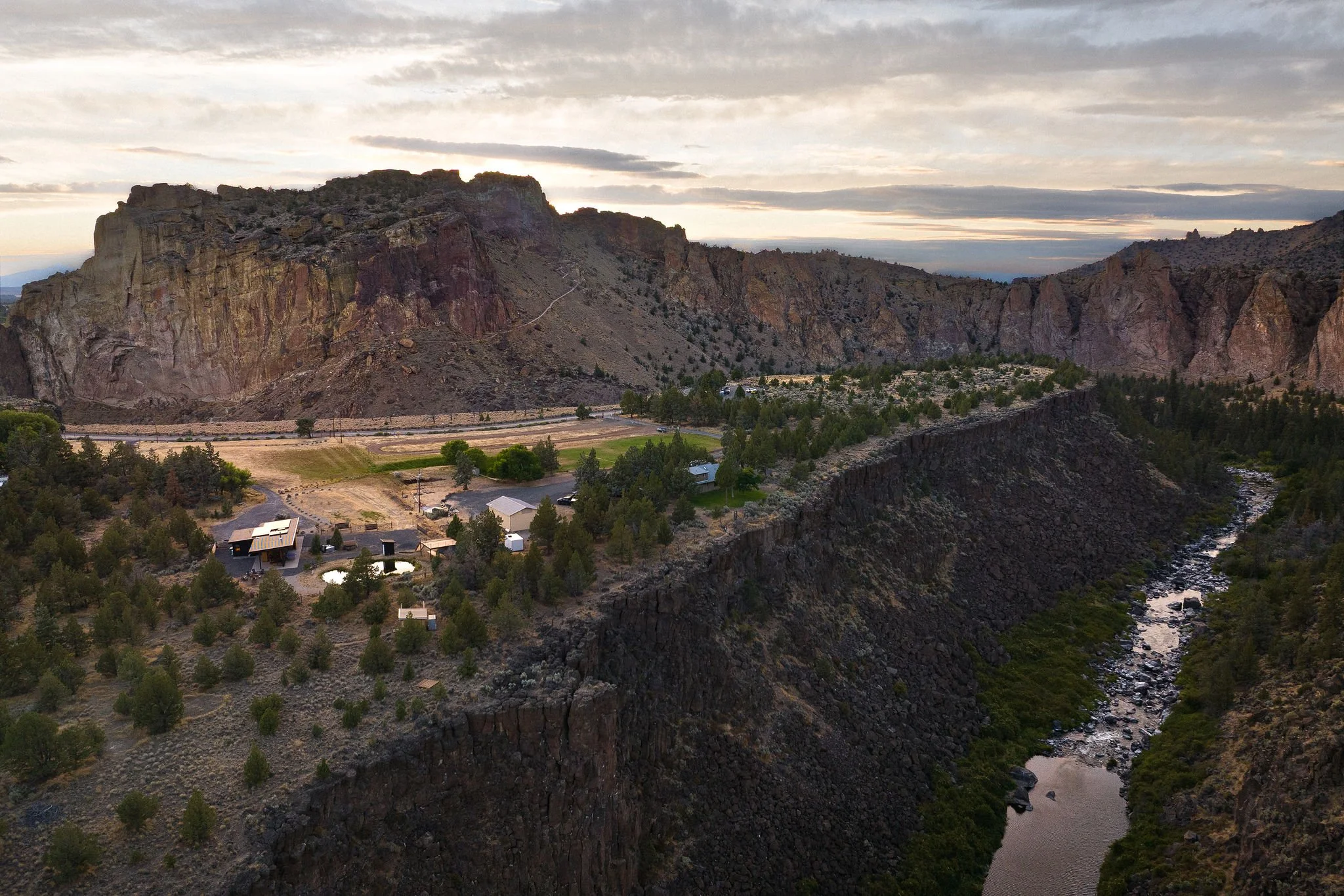 Landscape view of a canyon with a river running through it, surrounded by rocky cliffs and sparse trees, at sunset or sunrise.