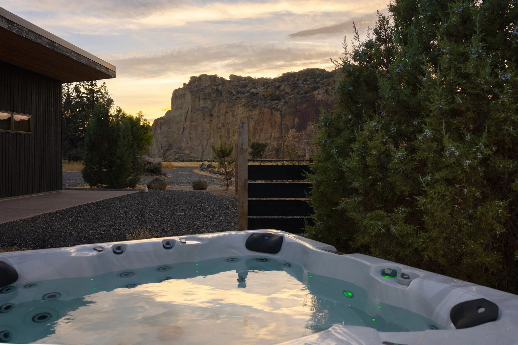 A hot tub filled with water outdoors at sunset, with a mountain in the background and trees surrounding the area.