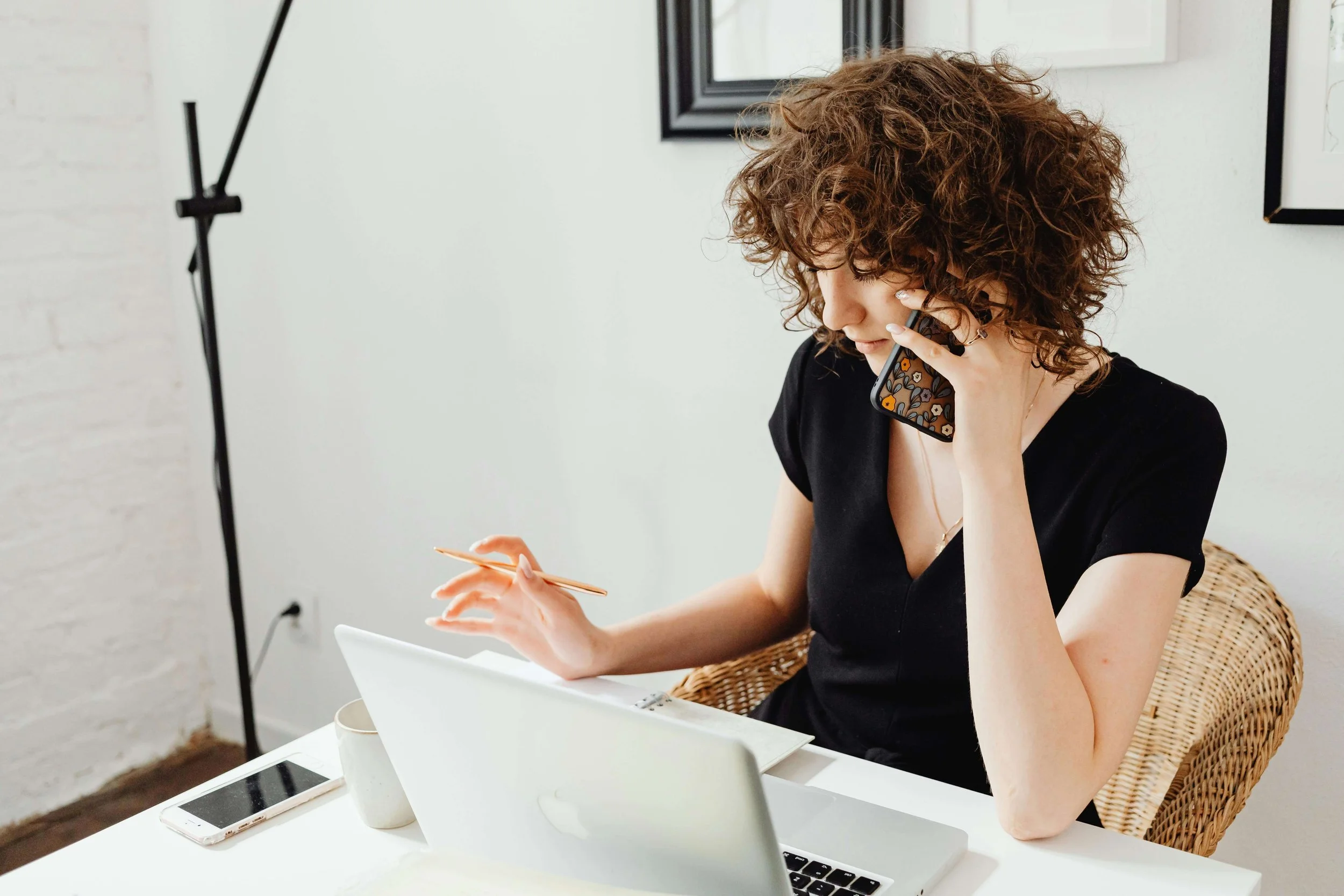 Woman sitting with laptop talking on phone and taking notes
