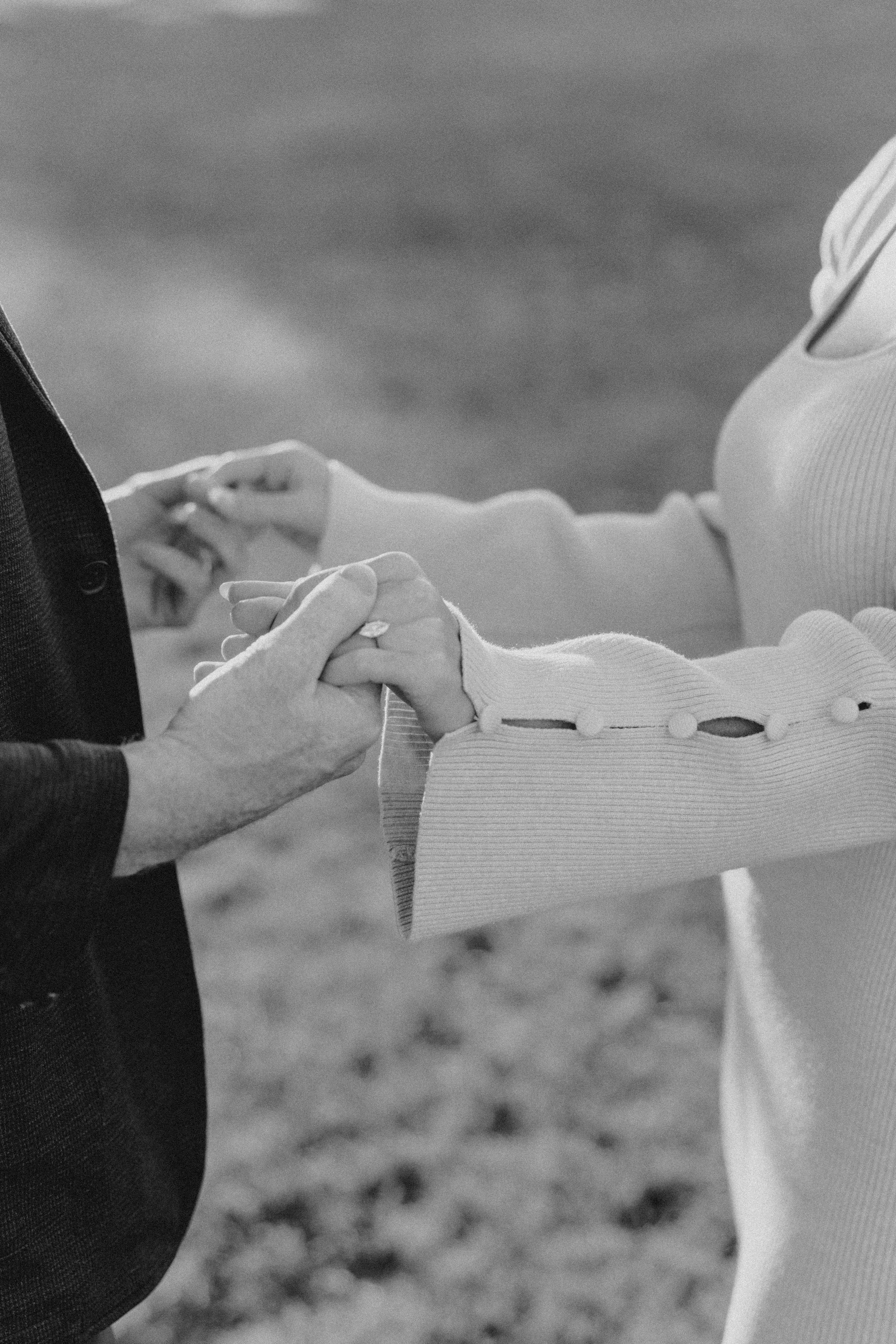A close-up black and white photo of a couple holding hands, with the woman's hand gently resting on the man's hand.