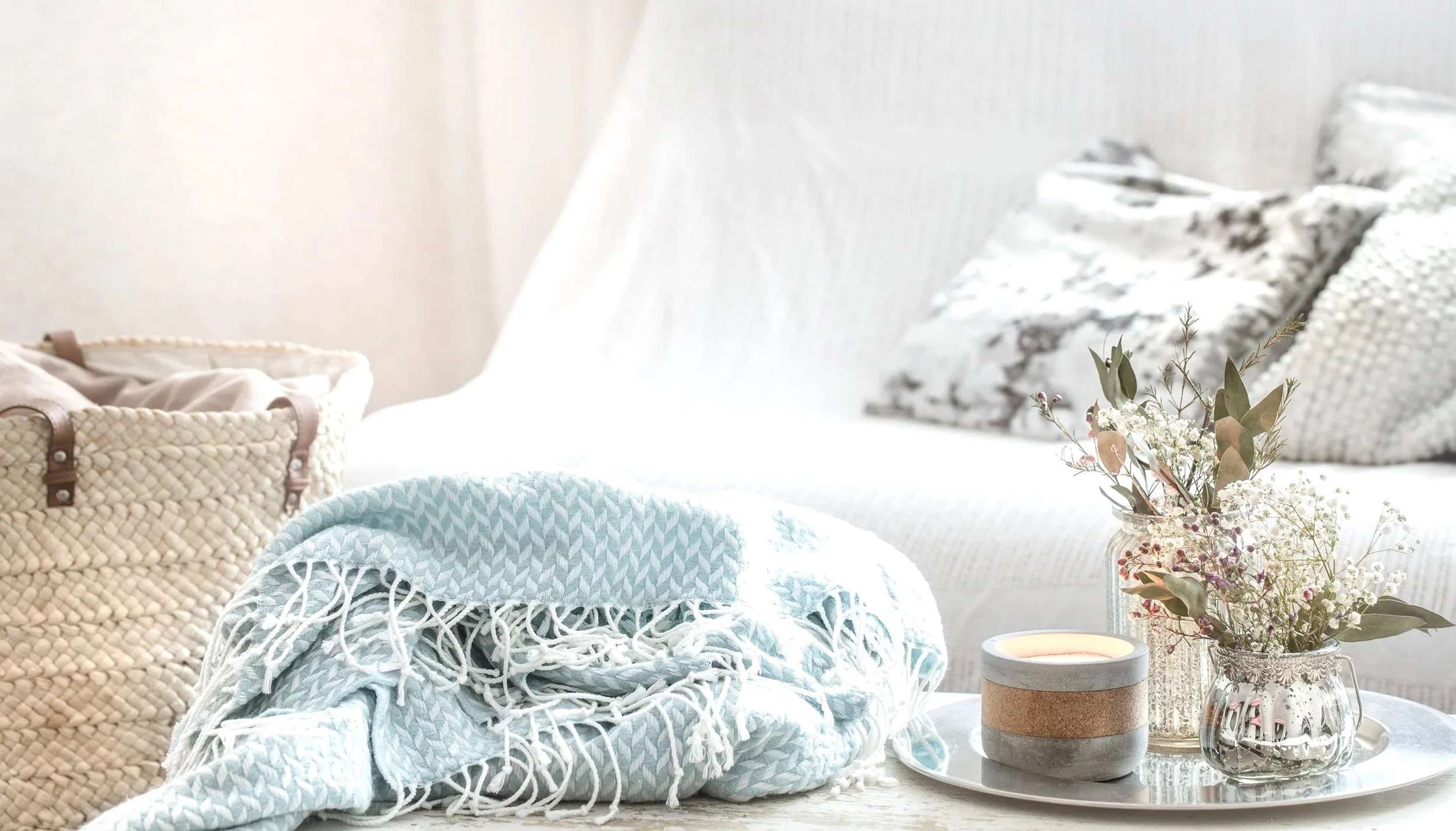 Living room with a white sofa, patterned pillows, a tray with a candle, and a vase of flowers