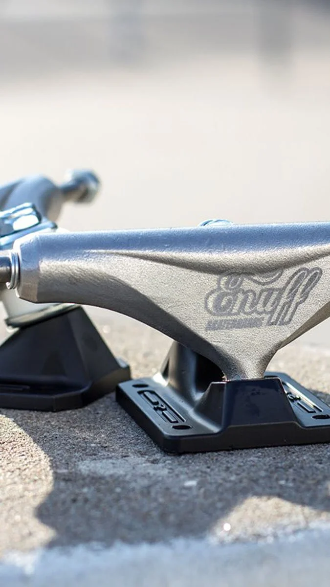 Close-up of a skateboard truck with the brand name Enuff, resting on a concrete surface with a slightly blurred background.