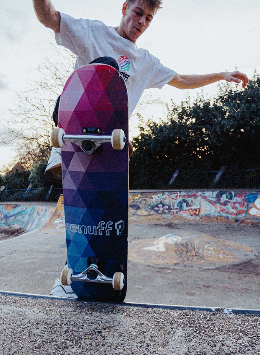 A young male skateboarder performing a trick at a skate park with graffiti, during sunset.