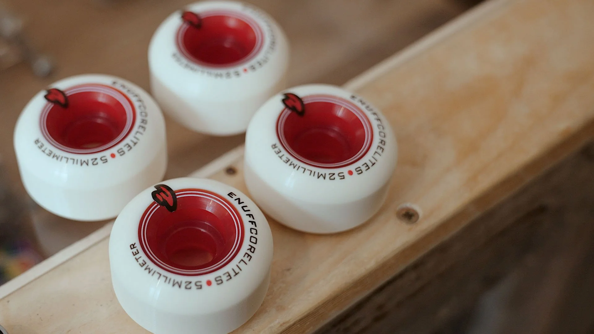 Four white roller skate wheels with red centers, arranged on a wooden surface.