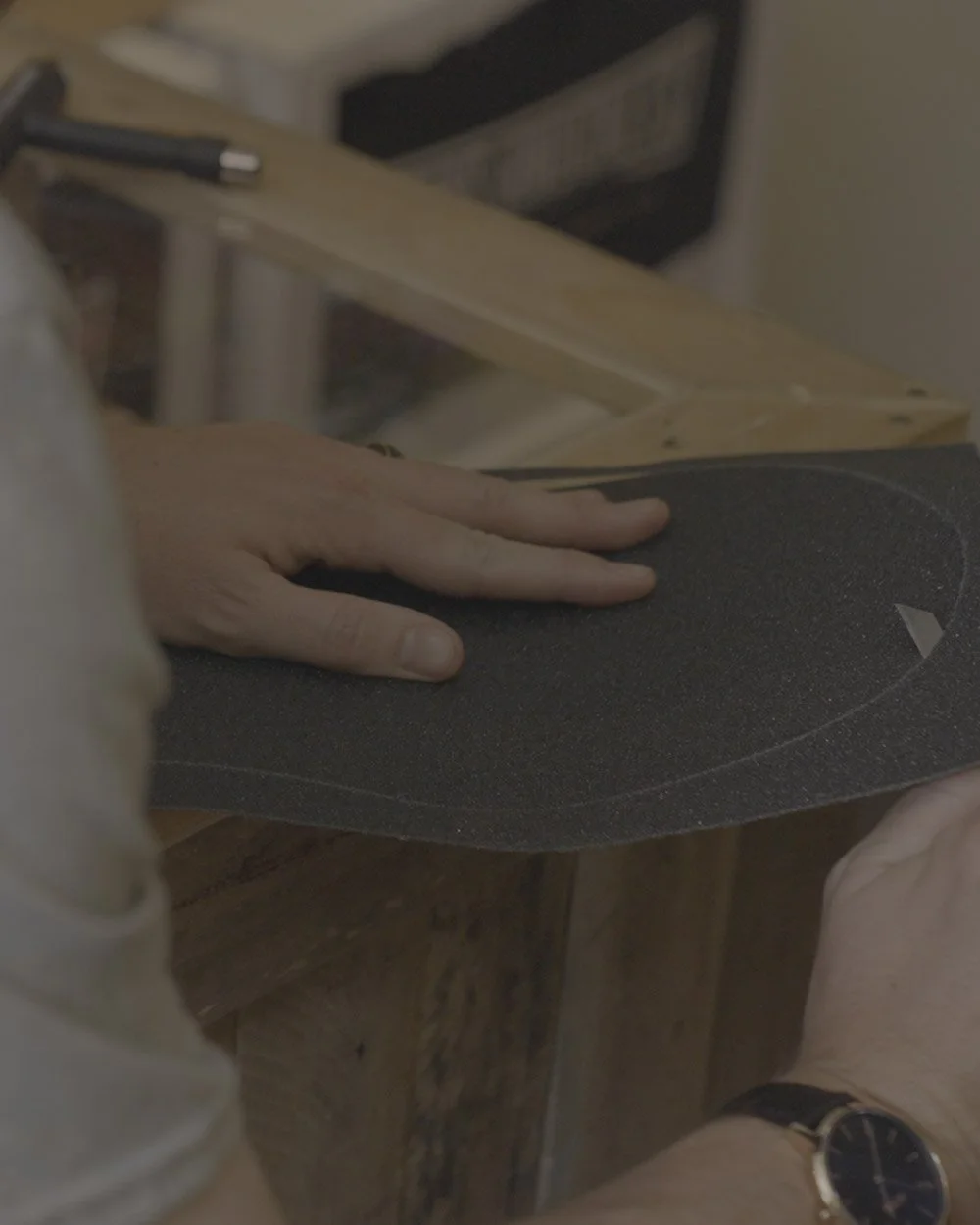 A person shaping a skateboard deck on a workbench with their hands.
