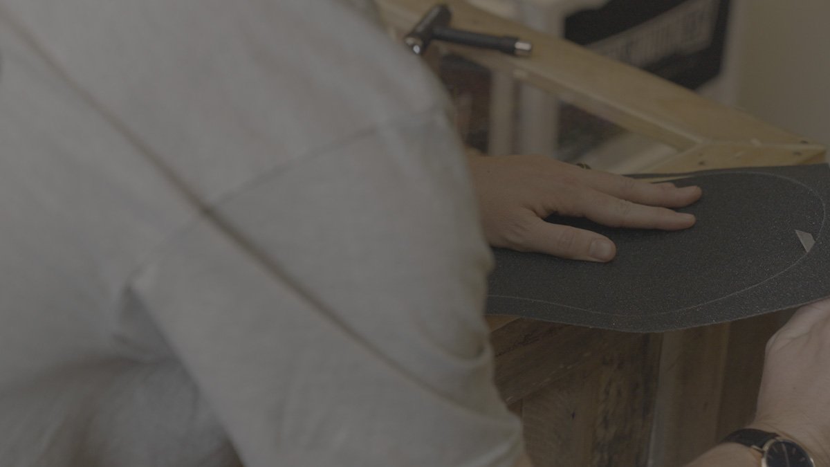 A person holding a skateboard deck in a workshop.