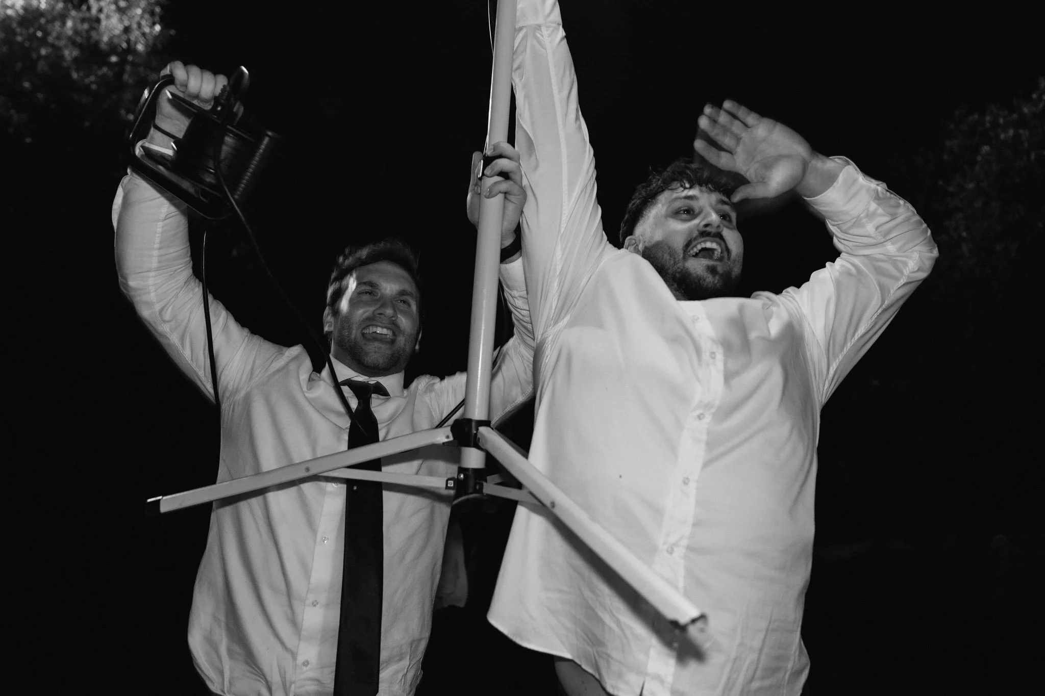 Due uomini sorridenti, uno con una bandiera, in piedi all'aperto di notte, uno con una macchina fotografica, entrambi in abiti formali