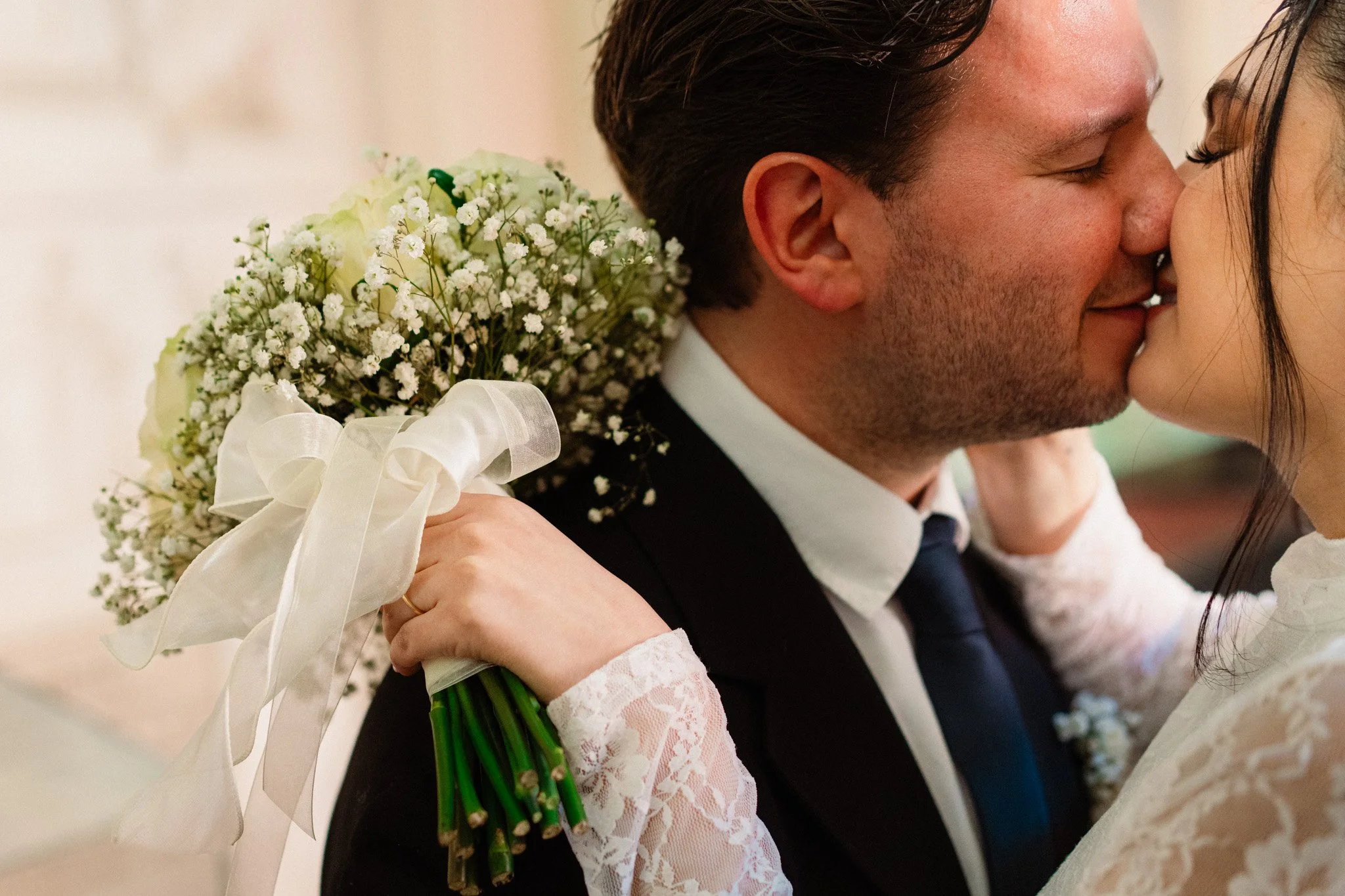 Una coppia di sposi si bacia durante il loro matrimonio, con un bouquet di fiori bianchi in mano.