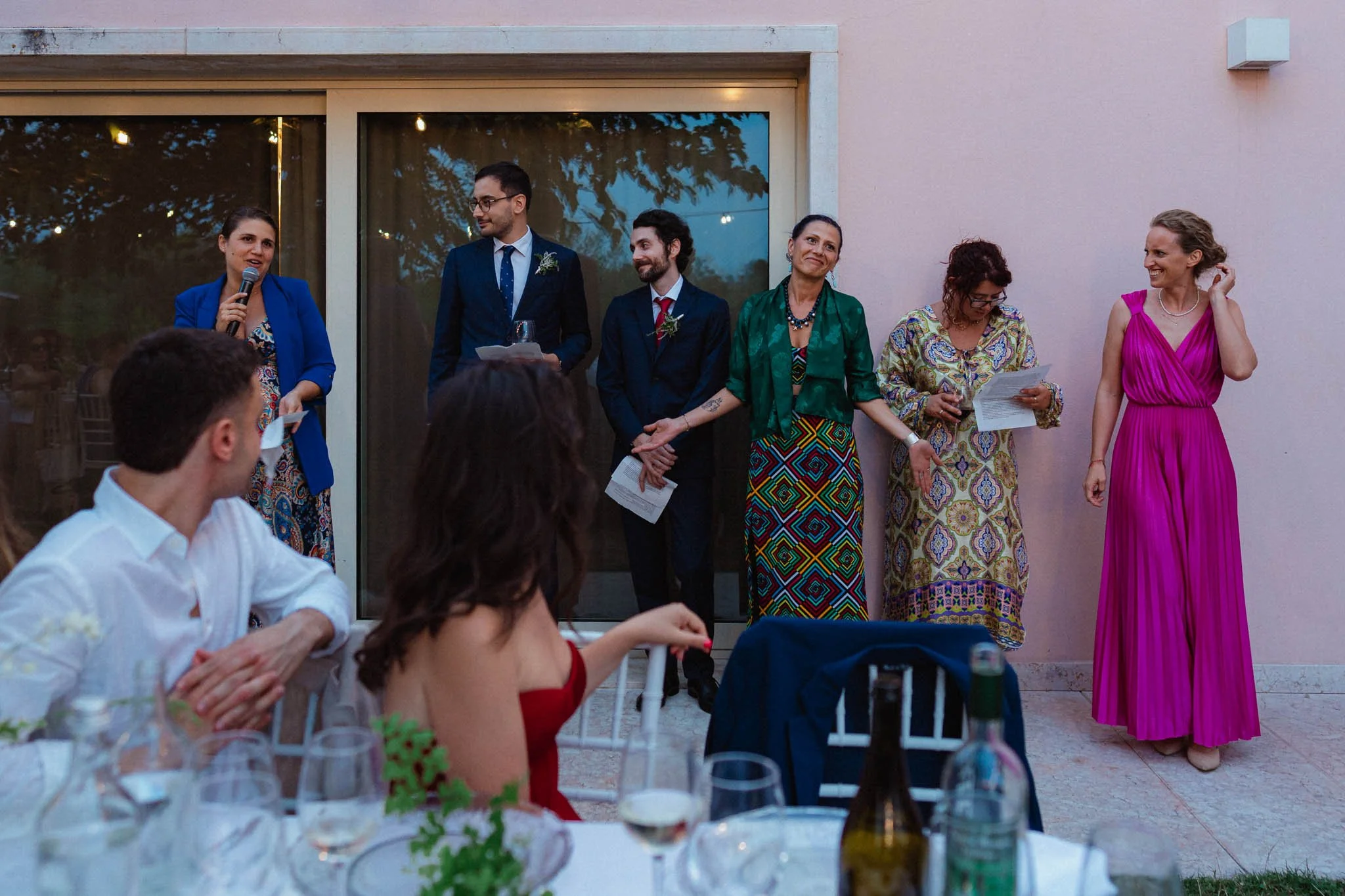 Giornata di matrimonio con un momento di discorso, con sei persone in piedi e due sedute che ascoltano, al tramonto in un giardino.