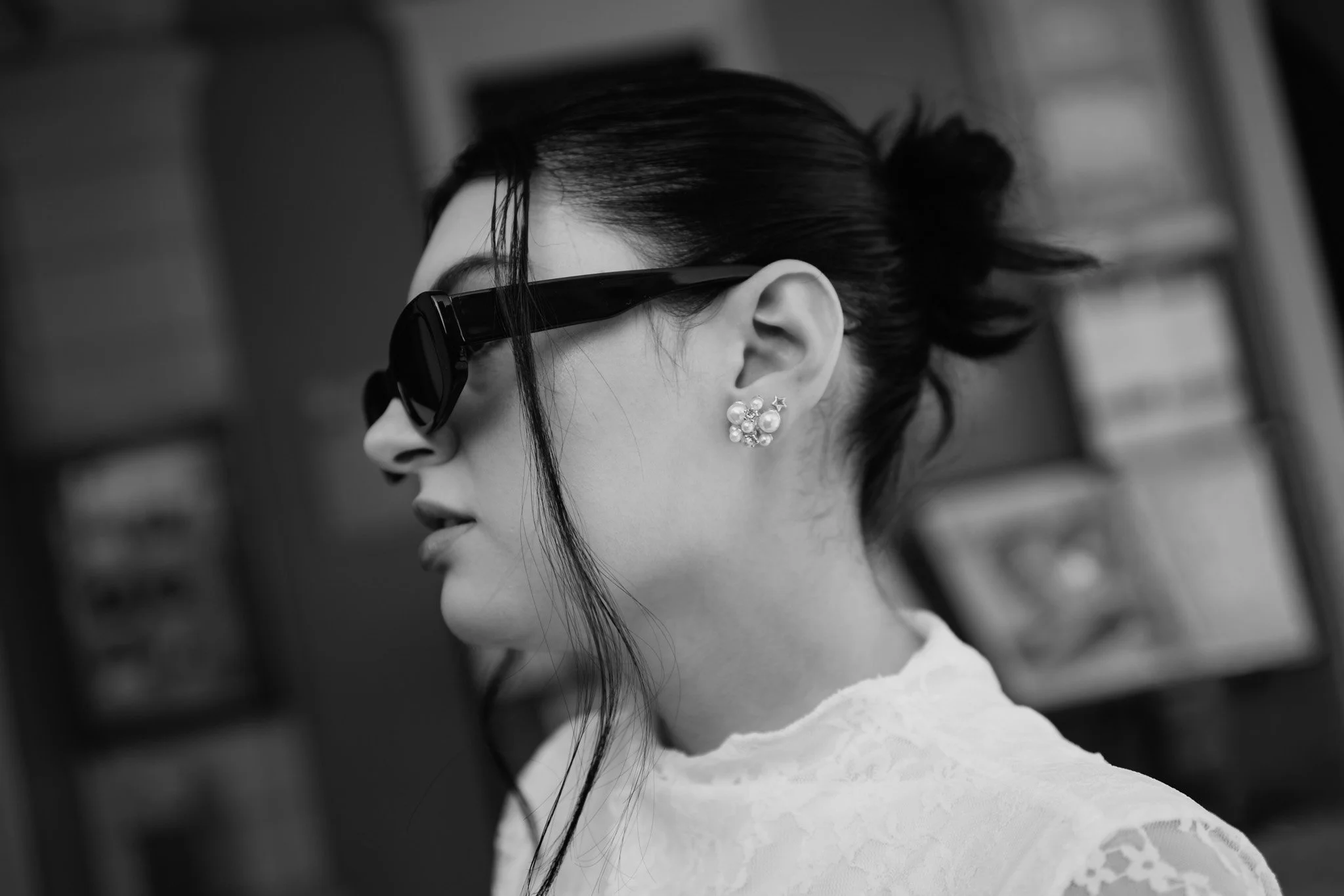 Ragazza con occhiali da sole neri e orecchini a fiore, con capelli scuri raccolti, vista di profilo in bianco e nero.