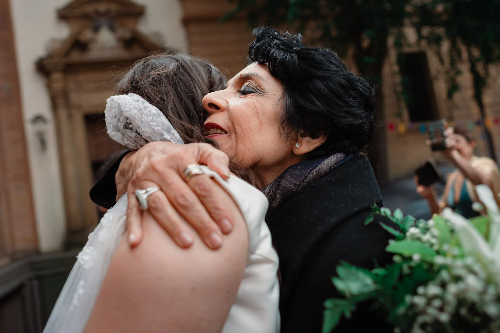 Due donne si abbracciano affettuosamente, probabilmente in un matrimonio o occasione speciale.