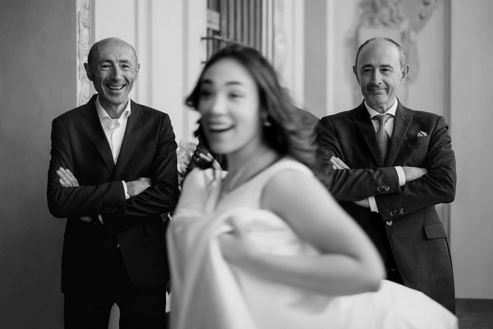 Tre persone sorridenti, due uomini in abiti formali e una donna in abito bianco, si trovano in un ambiente elegante, probabilmente un evento o una riunione.