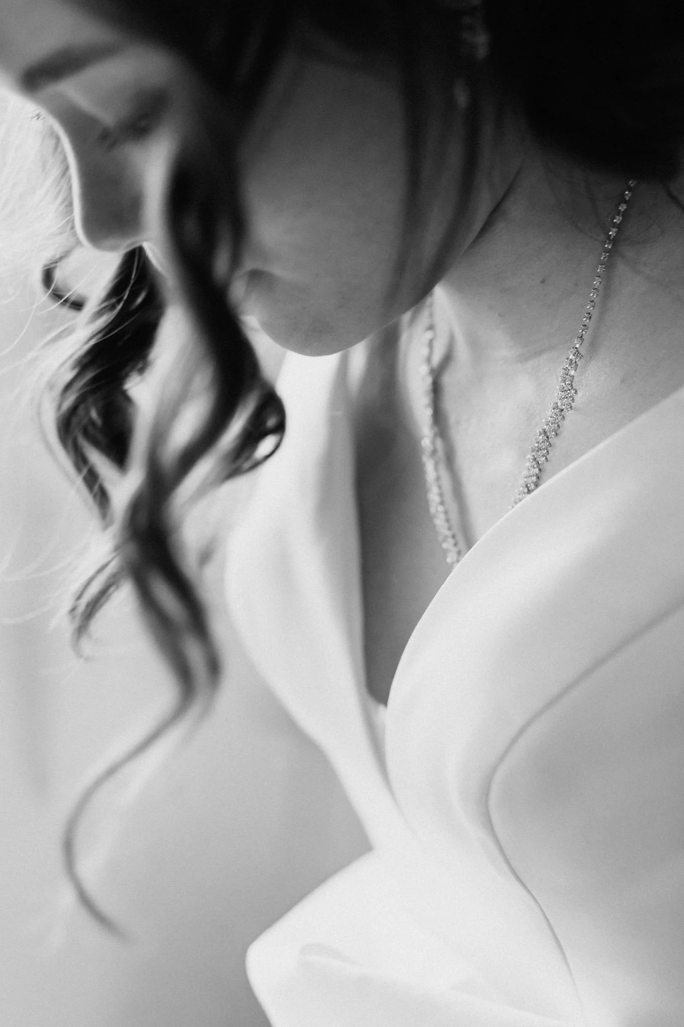 Sposa con capelli ricci che indossa una collana e un vestito bianco, con dettagli satinati.