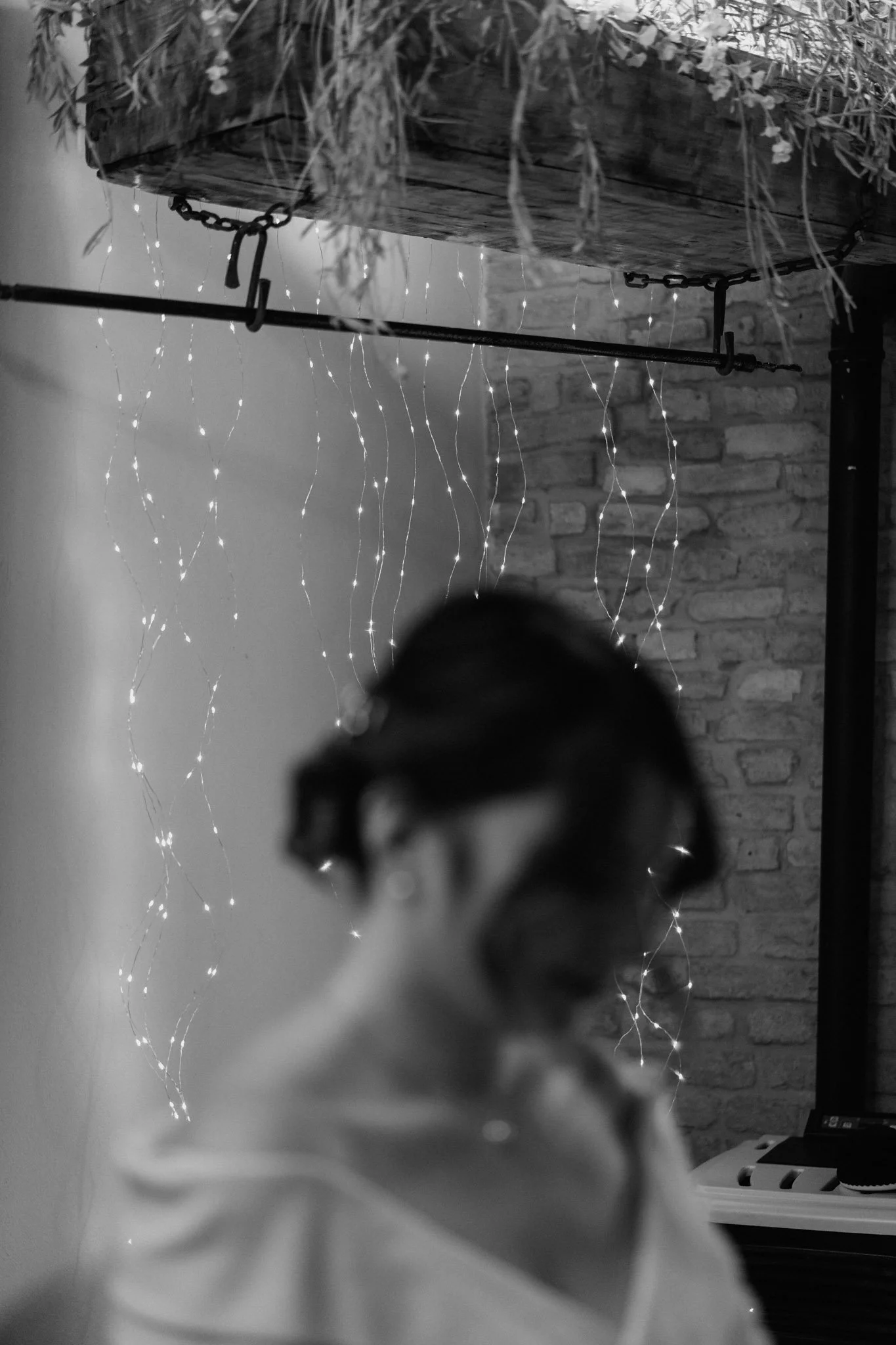 Immagine in bianco e nero di due persone che si abbracciano o si tengono per mano, con luci decorative in background e pareti di mattoni.