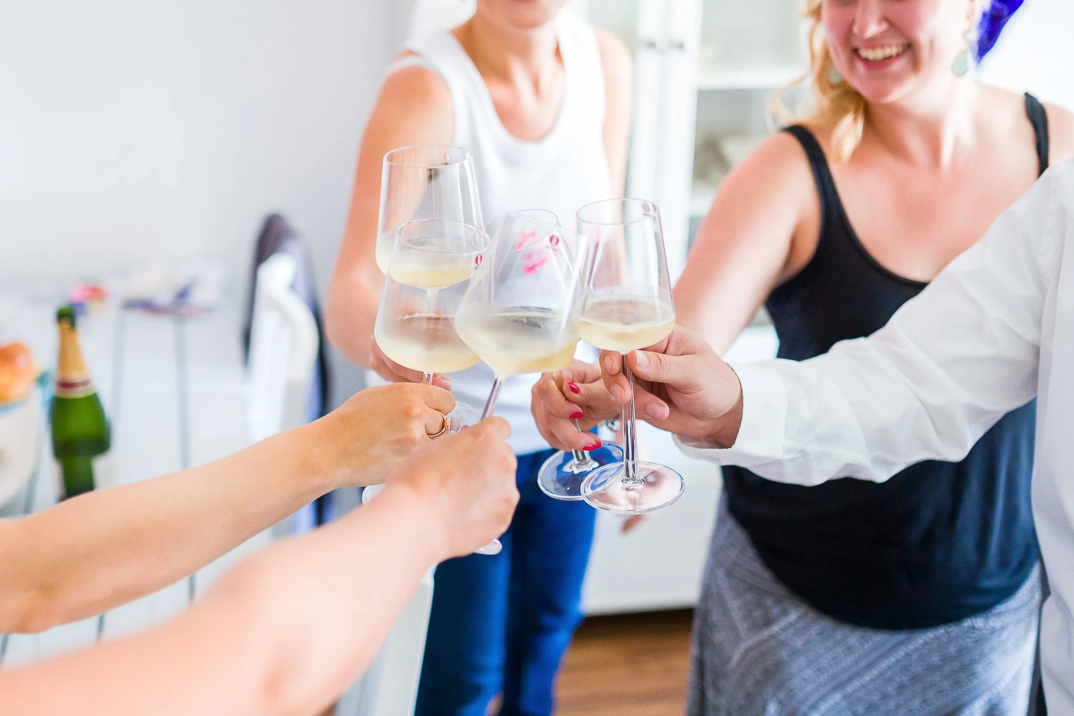 Mehrere Menschen stoßen mit Weingläsern an, die mit Weißwein gefüllt sind, bei einer Feier oder Zusammenkunft.