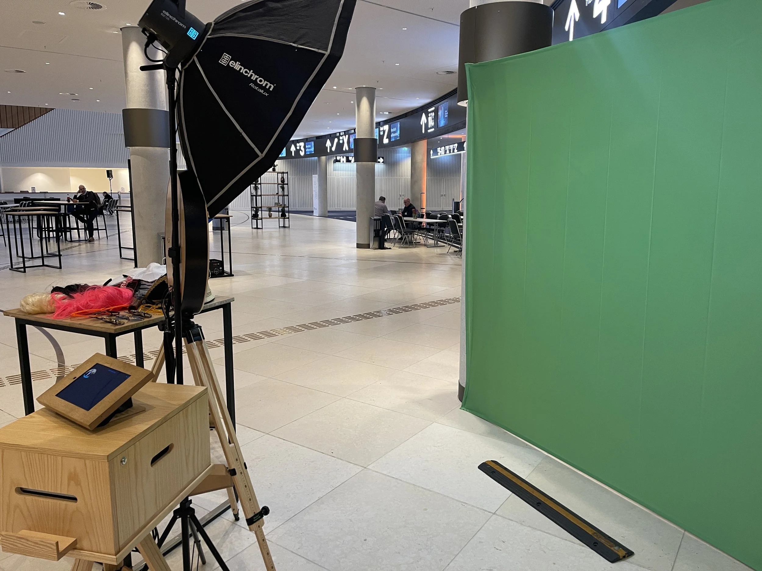 Fotostudio-Setup mit grünem Hintergrund, Softbox-Licht, Tisch mit Requisiten und einem Monitor in einer großen Halle.