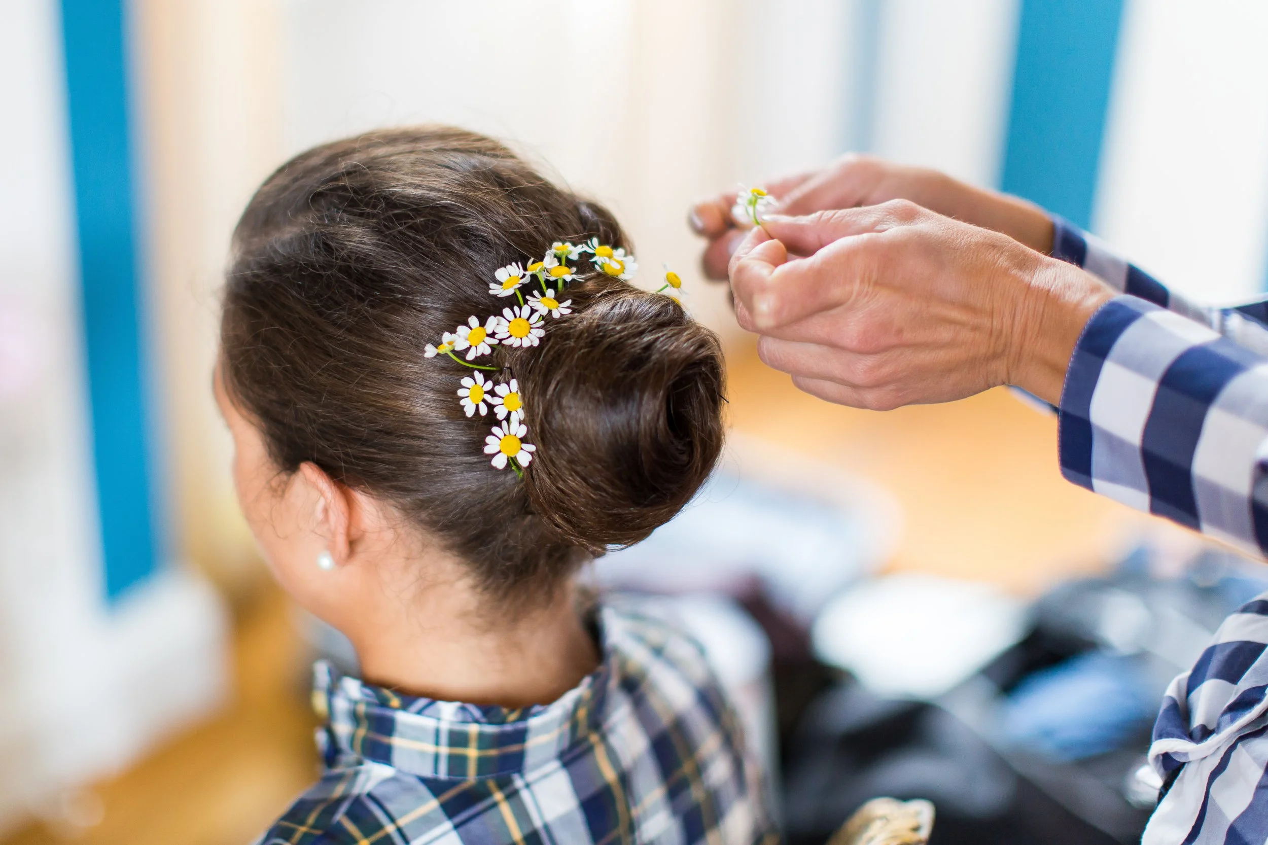 Eine junge Frau erhält eine Haarfrisur mit kleinen weißen Blumen als Dekoration. Sie trägt ein kariertes Hemd.