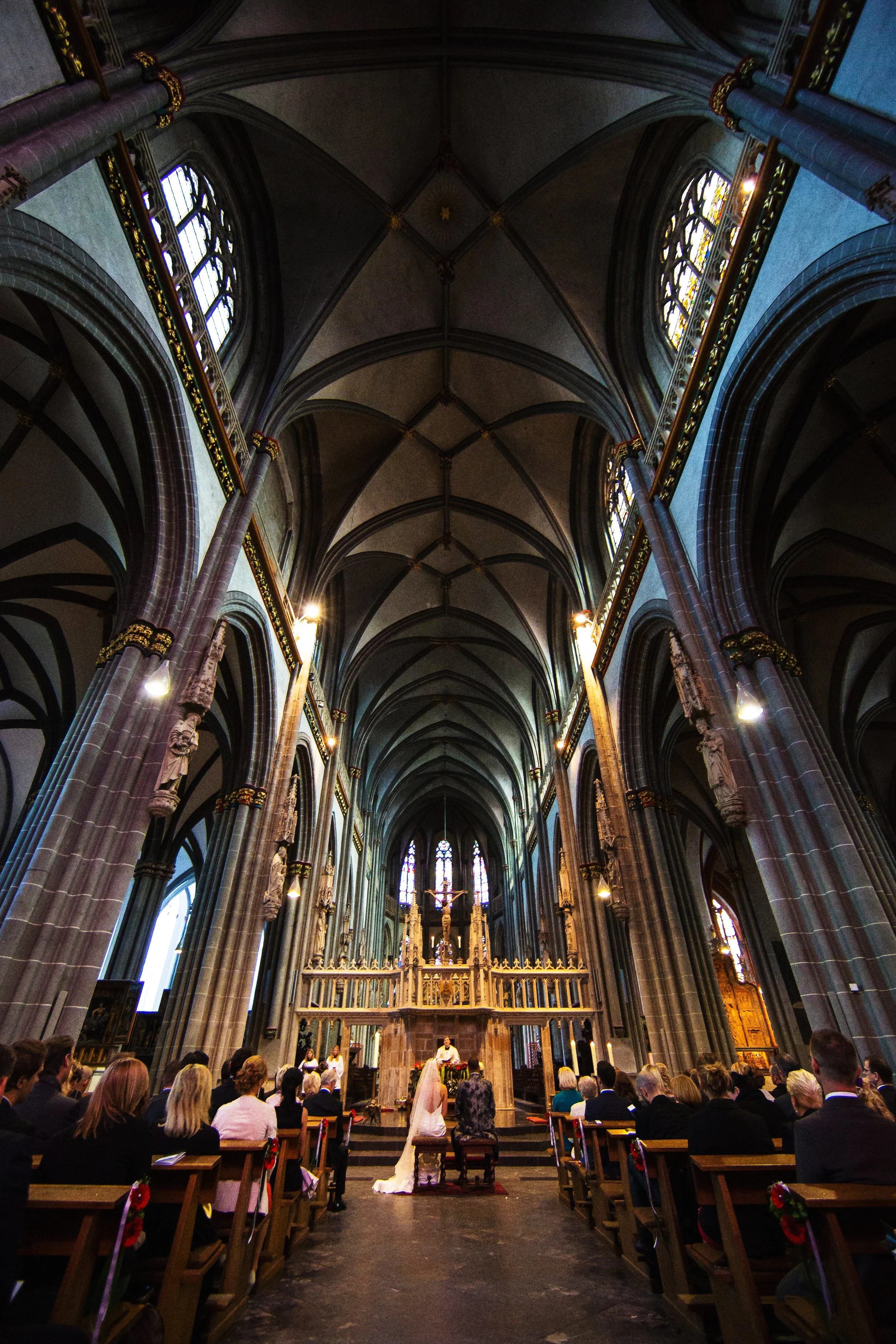 Innenansicht einer gotischen Kirche ( Damo Xanten) während einer Hochzeitszeremonie mit Braut und Bräutigam vor dem Altar, umgeben von Gästen.