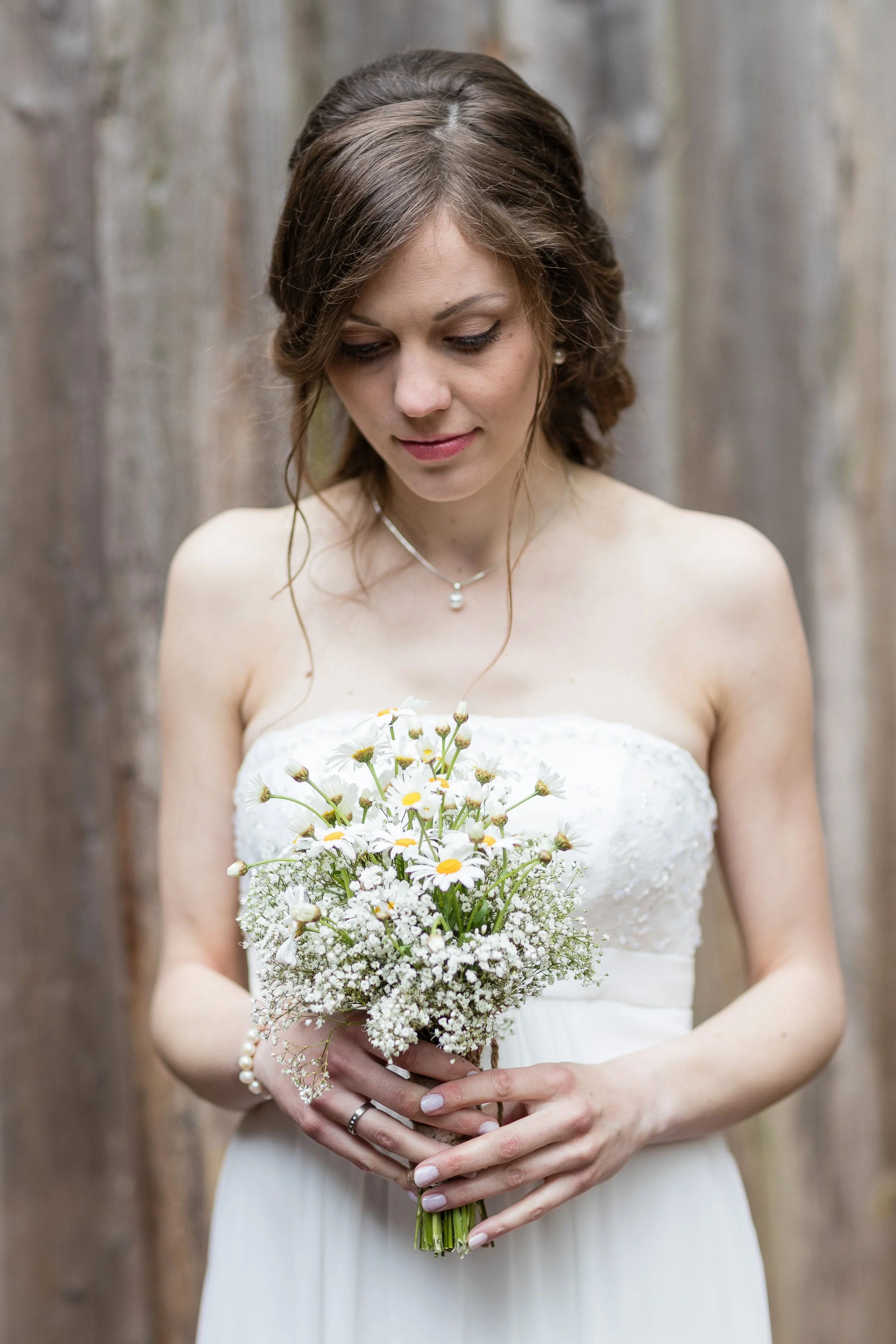 Junge Frau in einem weißen Kleid hält einen Strauß aus weißen Blumen vor einer Holzvertäfelung.