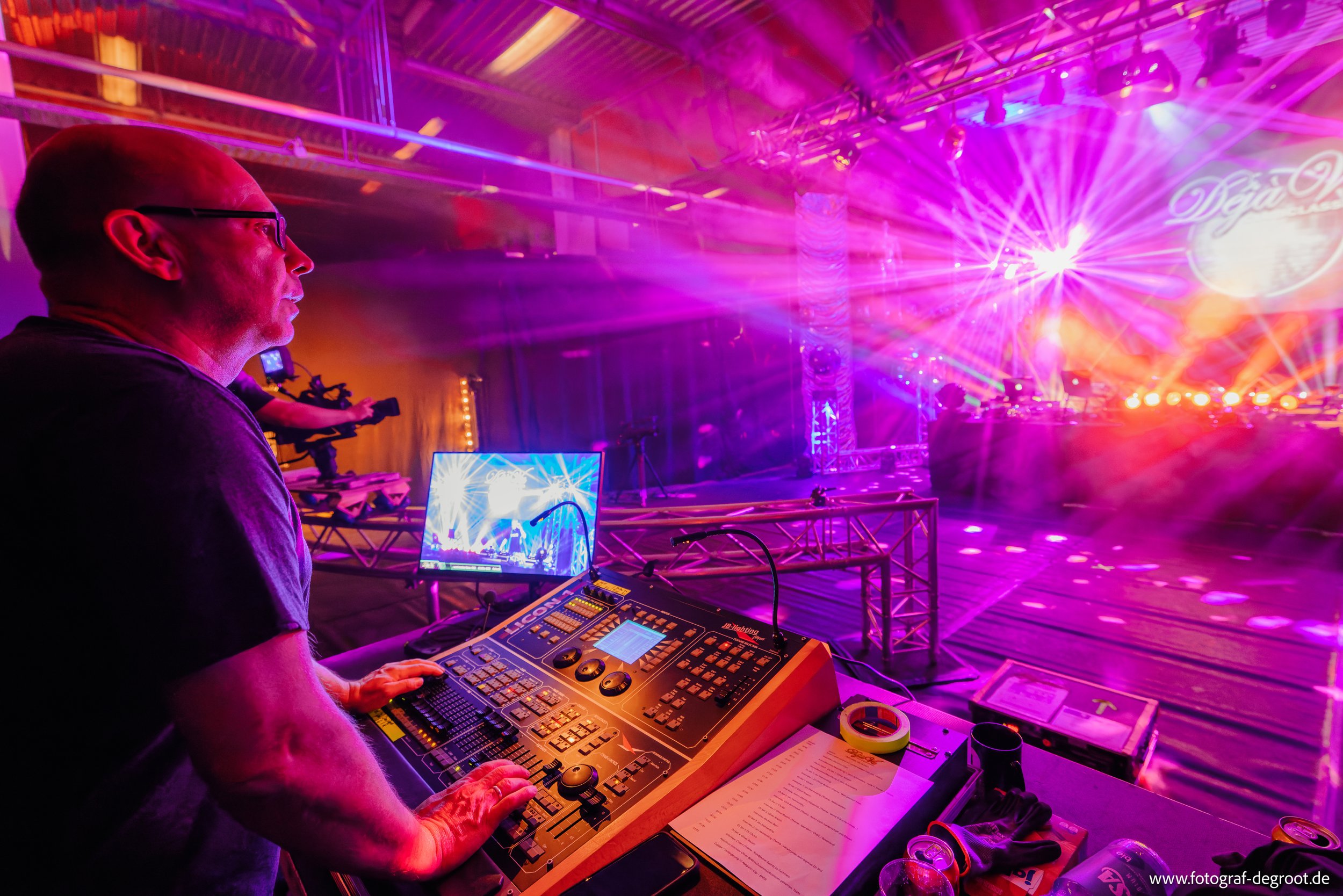Mann steuert Lichttechnik bei einem Event mit bunten Lichtern und einer Bühne.