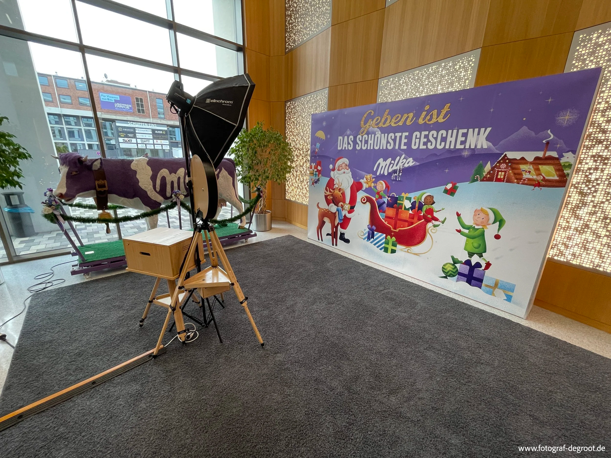 Fotografie eines weihnachtlichen Setups mit einem Rentier, einer Weihnachtsnachricht im Hintergrund und einem Studiolicht in einem Raum mit großen Fenstern und Holzwänden.