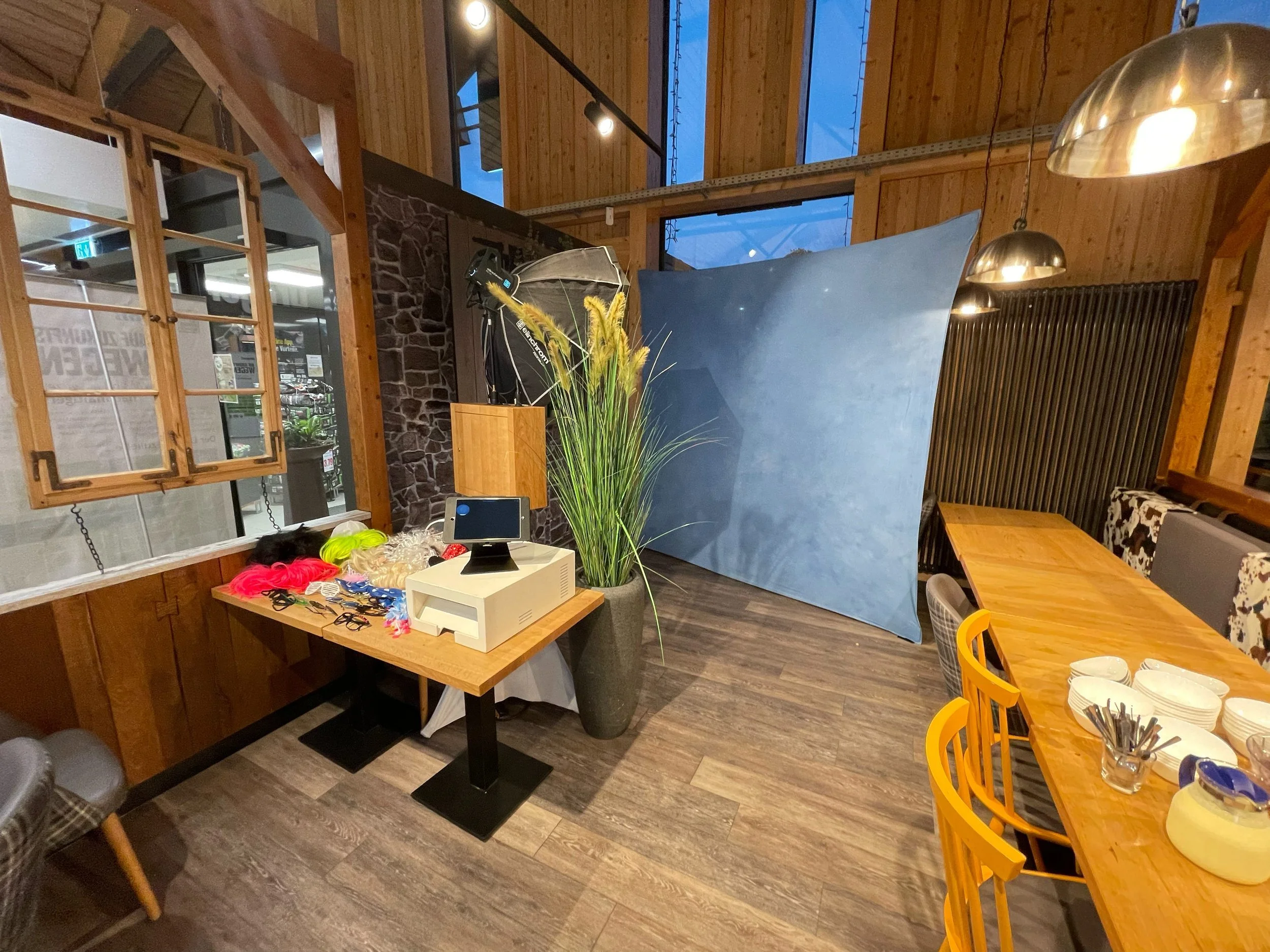 Innenraum eines Restaurants oder Cafés mit Holzwänden, Tischplatten und Stühlen, Fotostudioausrüstung wie Hintergrund, Licht und Dekoration, sowie einem Computer und Material für Fotoshootings.