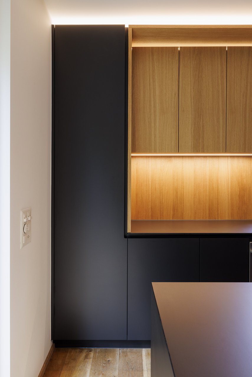 Modernes Kücheninterieur mit schwarzen und hölzernen Schränken, integrierter Beleuchtung, Holzfußboden.