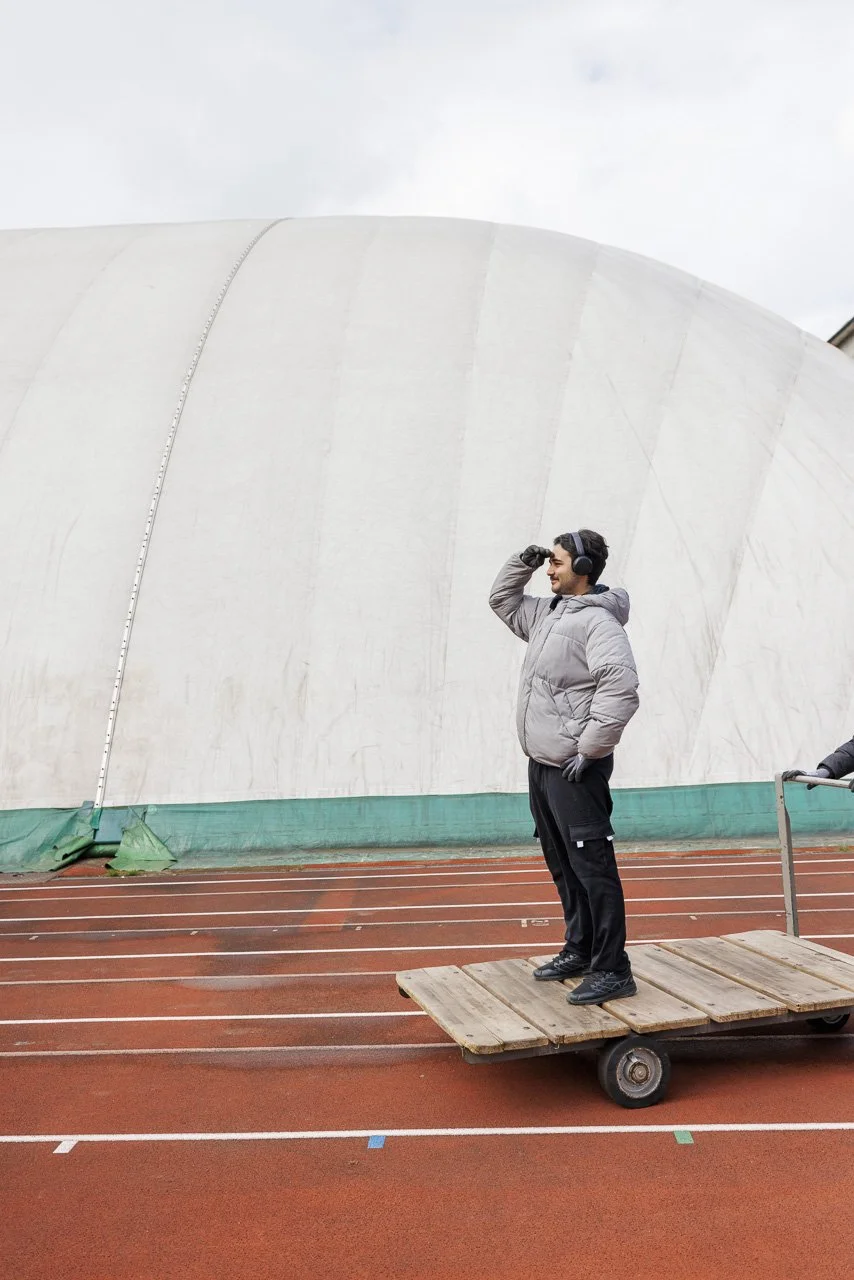 Mann steht auf einer flachen Palette auf einer Laufbahn, trägt eine gepolsterte Jacke und trägt Kopfhörer, während er nach oben schaut.