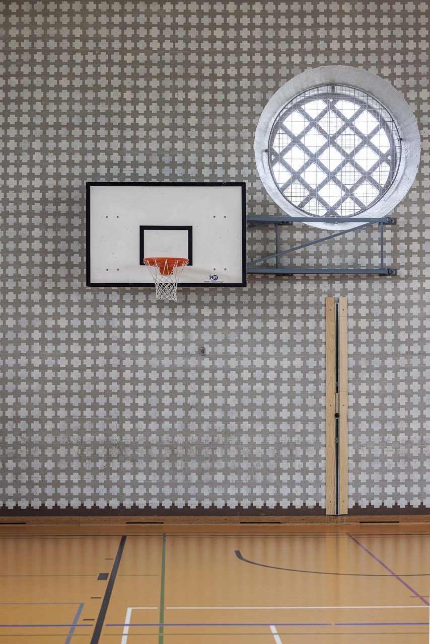 Innenansicht eines Basketballfelds mit einer Basketballkonstruktion an der Wand, einem Fenster mit Gitter, einem Holzreifen, einer Wandhalterung und einem Klemmbrett.