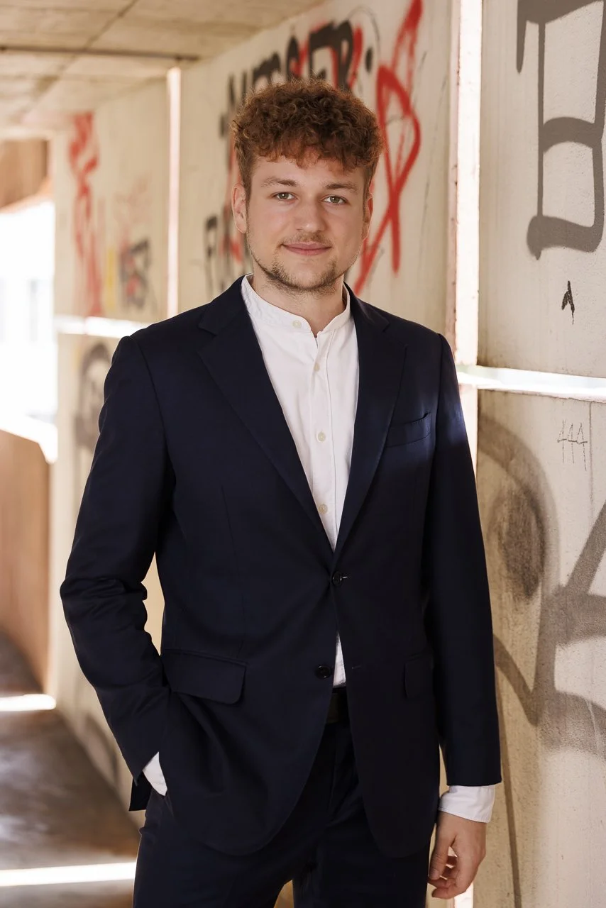 Junger Mann in dunklem Anzug und weißem Hemd, stehend vor einer bemalten Wand in einer urbanen Umgebung