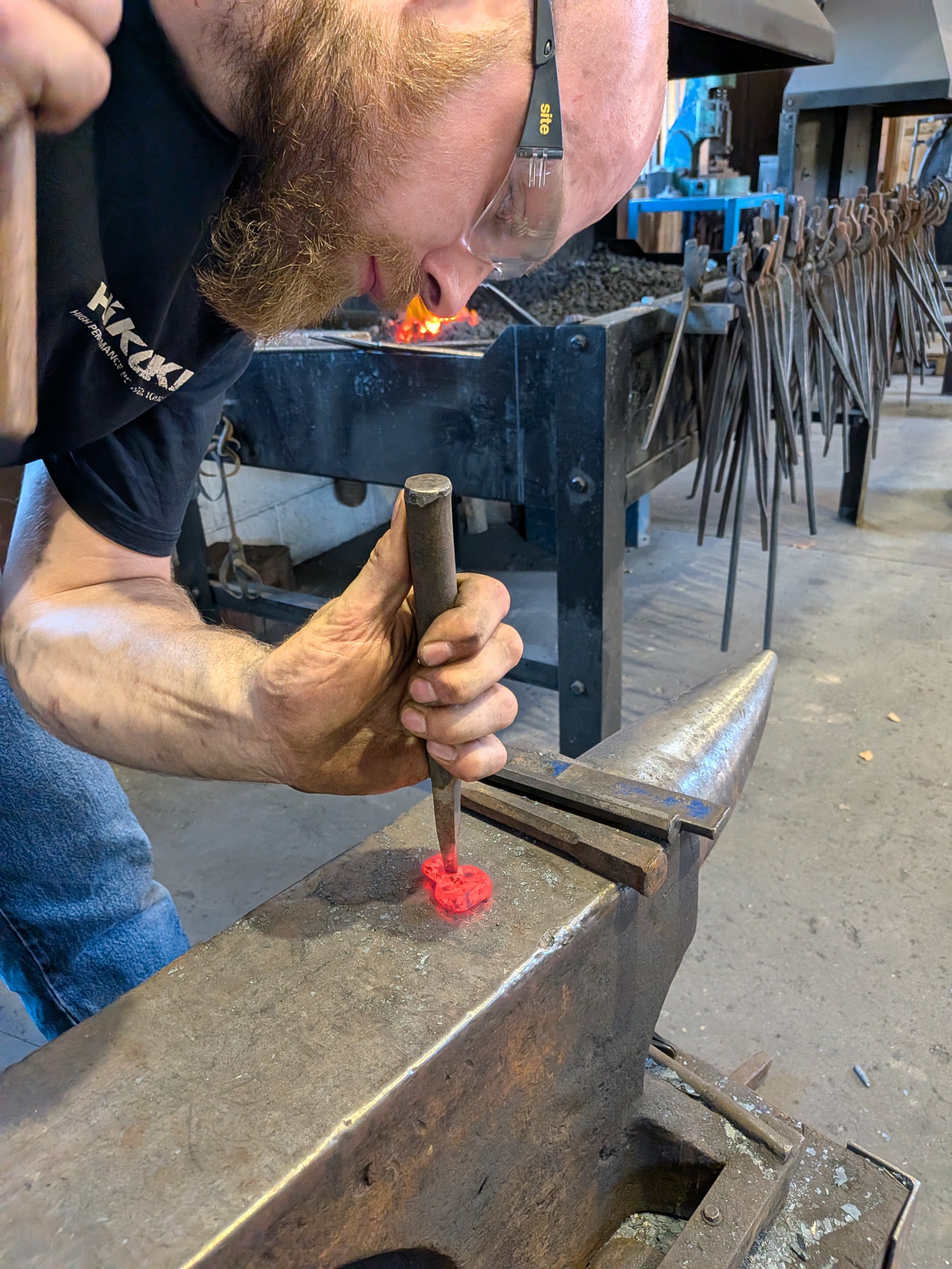 A blacksmith using a punch to add detail to a skull shaped keyring