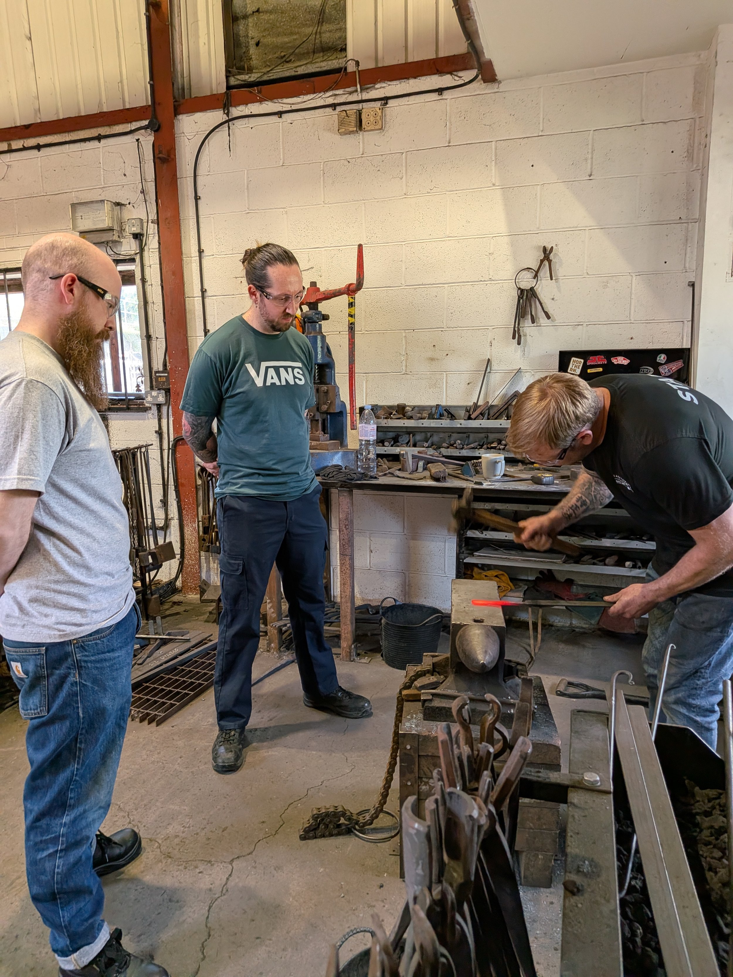 A blacksmith is showing students how to forge a a set down followed by a square taper to form the handle of a scroll knife.