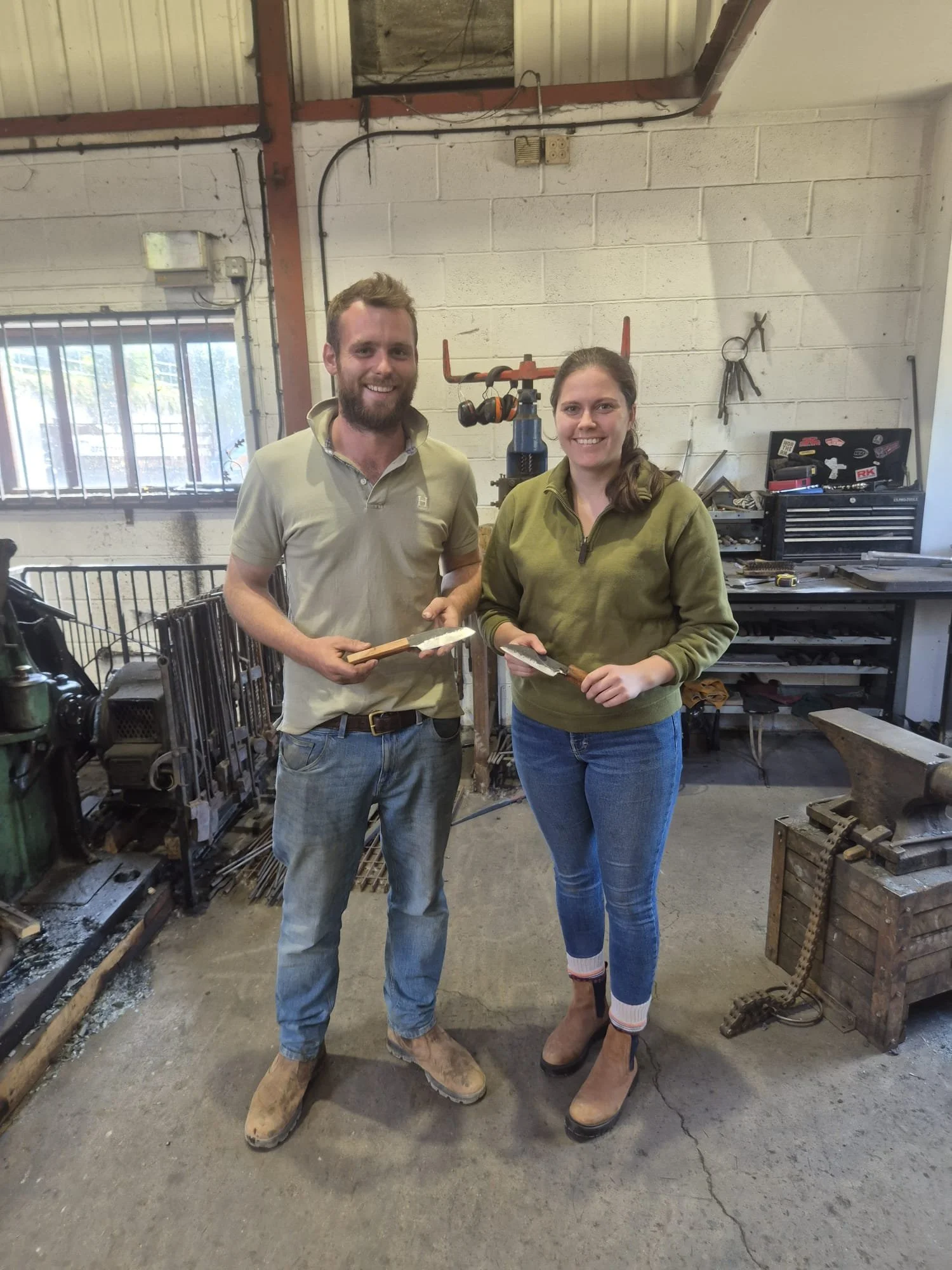 A happy couple holding their hand-forged knives that they just made